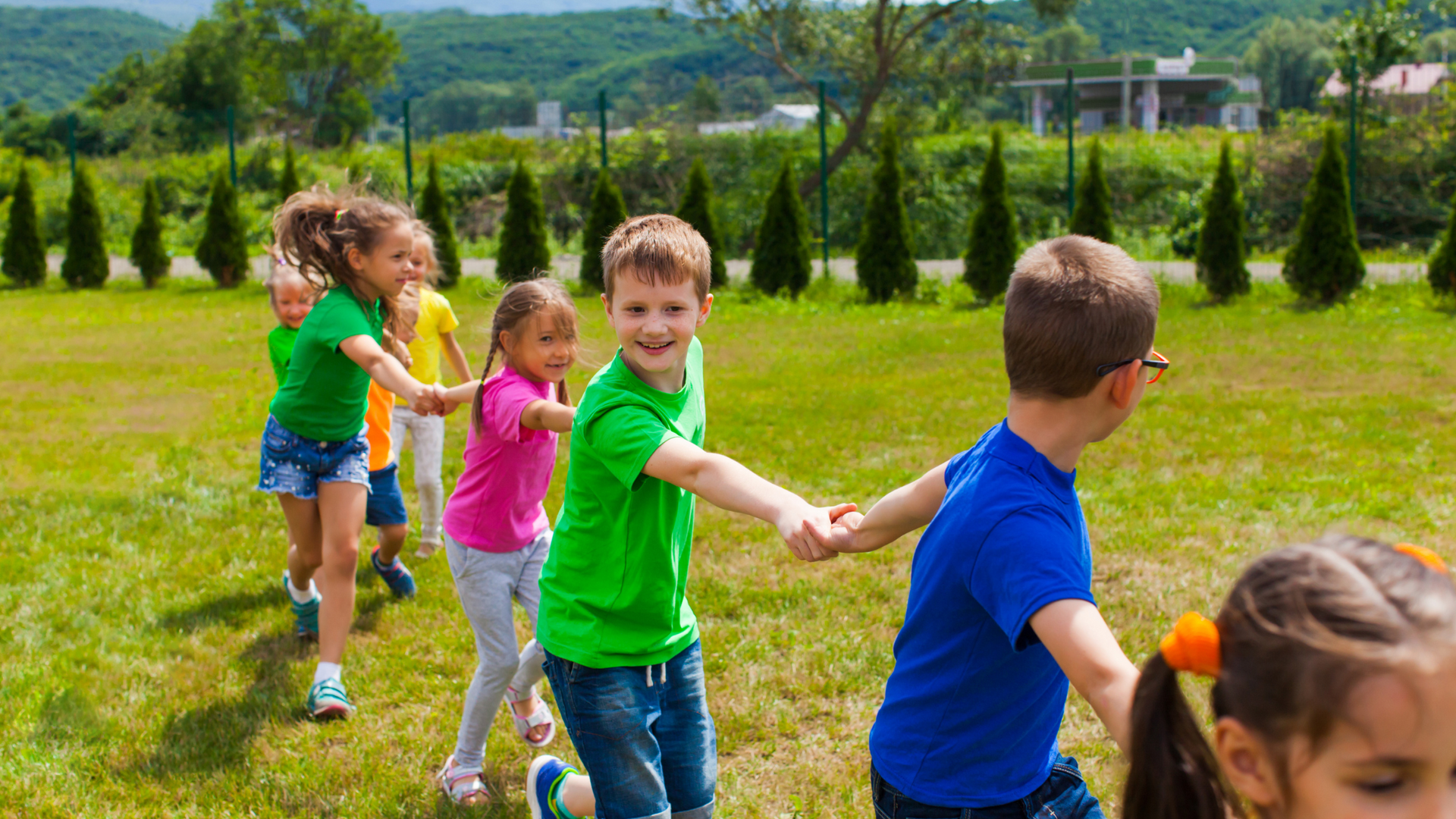 A group of children are holding hands in a circle in the grass.