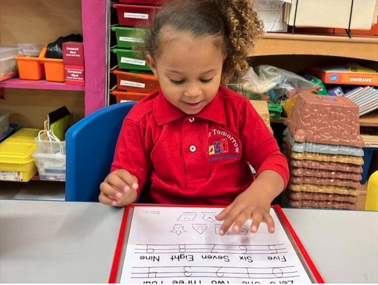 A little girl in a red shirt is writing on a piece of paper