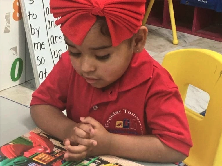 A little girl wearing a red shirt and a red bow is reading a book
