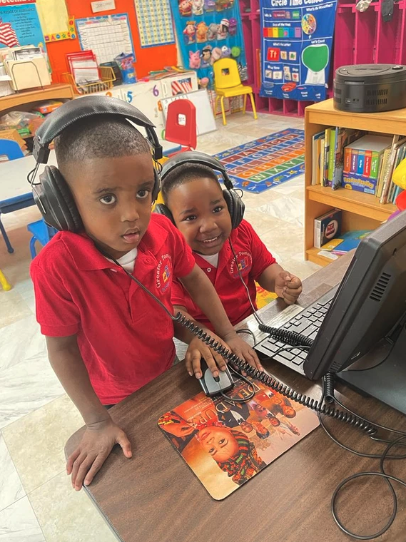 Two young boys wearing headphones are using a computer in a classroom