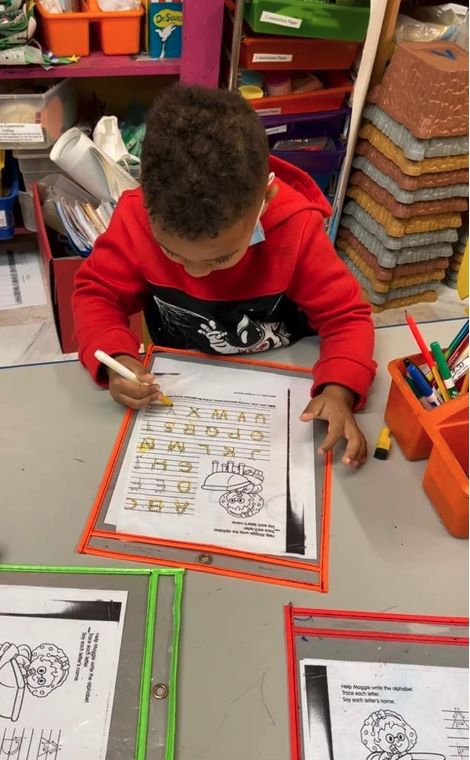 A young boy is sitting at a table writing on a piece of paper.