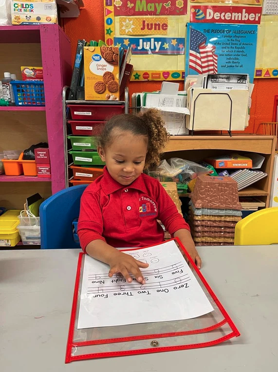 A little girl is sitting at a table in a classroom looking at a piece of paper.