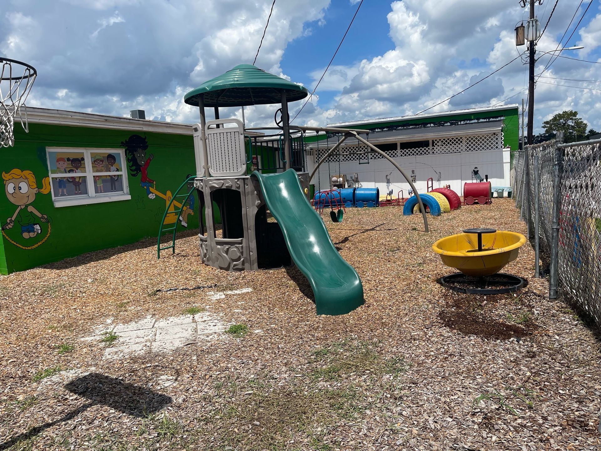 A playground with a slide and swings in front of a green building.