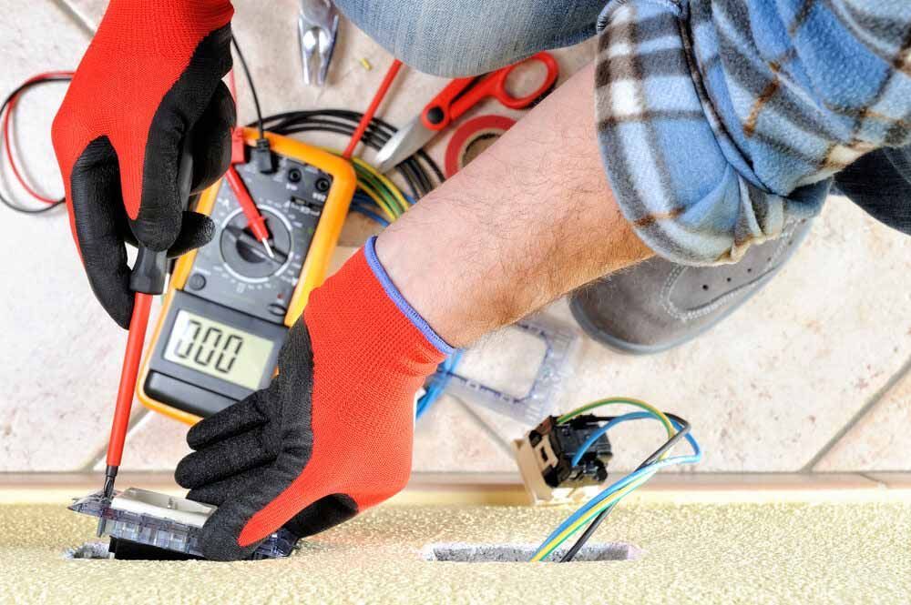 A Man Is Using A Multimeter To Test An Electrical Outlet — IPOWER Industries In Airlie Beach, QLD