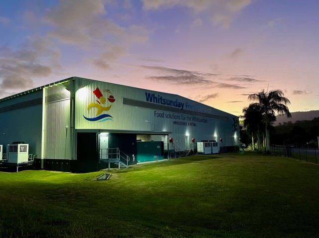 A Large Building Is Lit Up At Night With A Sunset In The Background — IPOWER Industries In Cannonvale, QLD