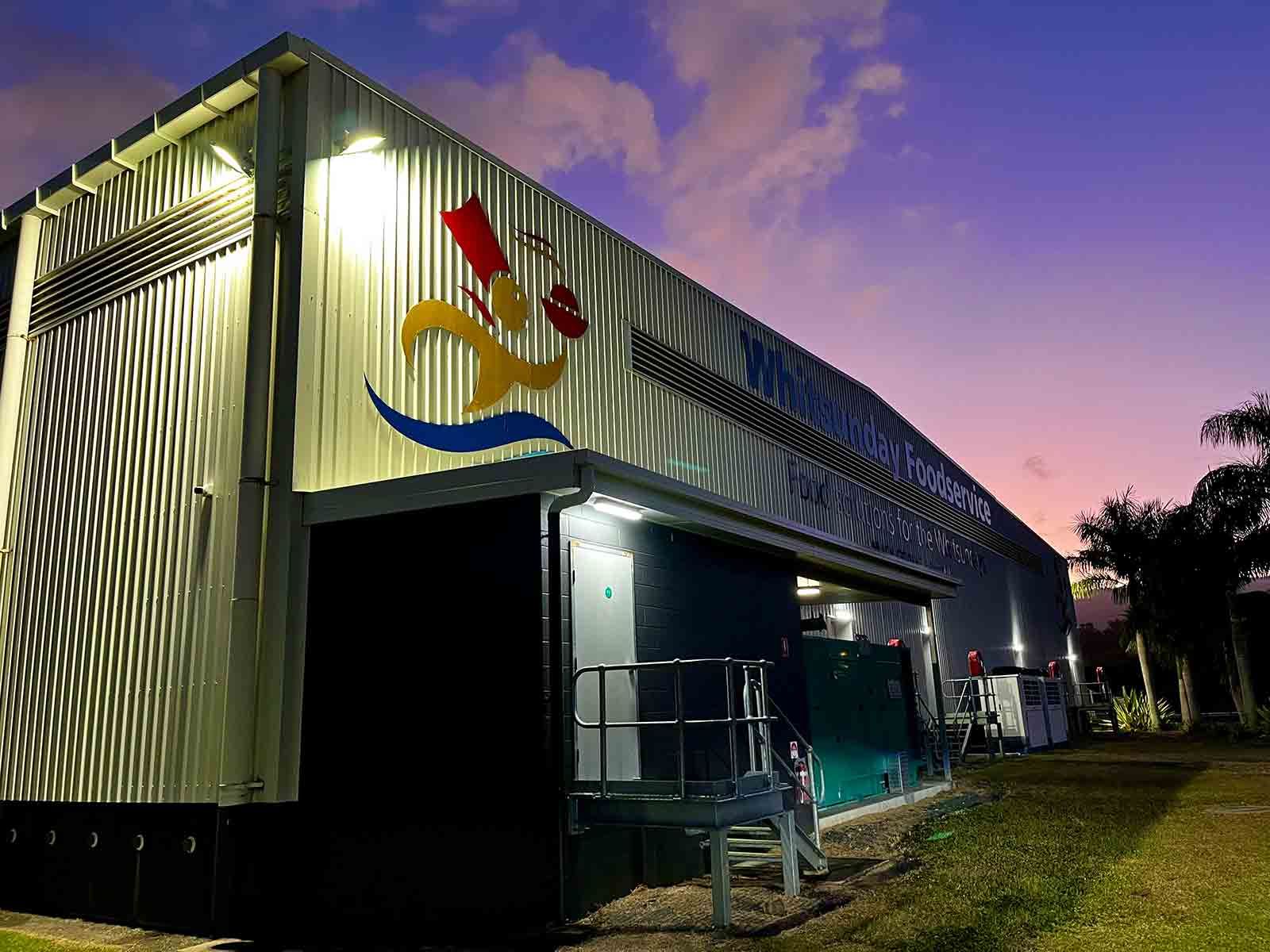 A Large Building With A Painting On The Side Of It Is Lit Up At Night — IPOWER Industries In Bowen, QLD