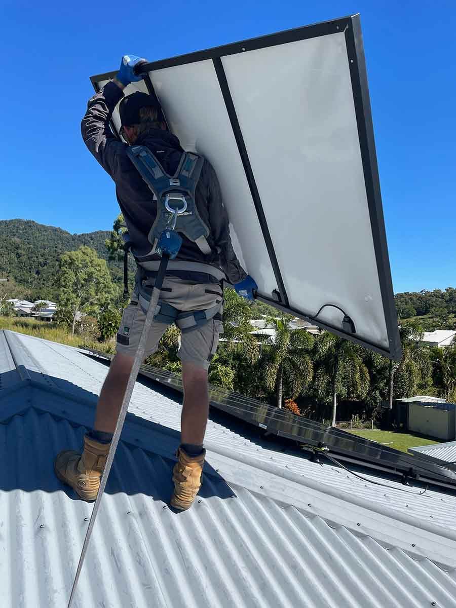 A Man Is Standing On Top Of A Roof Holding A Solar Panel — IPOWER Industries In Cannonvale, QLD