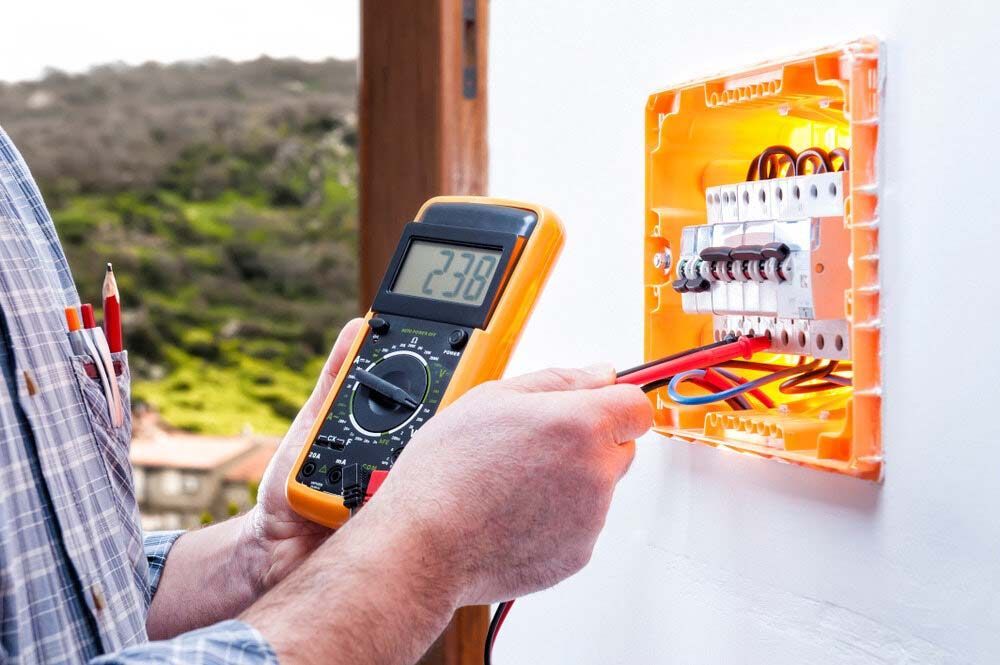 A Man Is Using A Digital Multimeter To Test An Electrical Box — IPOWER Industries In Cannonvale, QLD