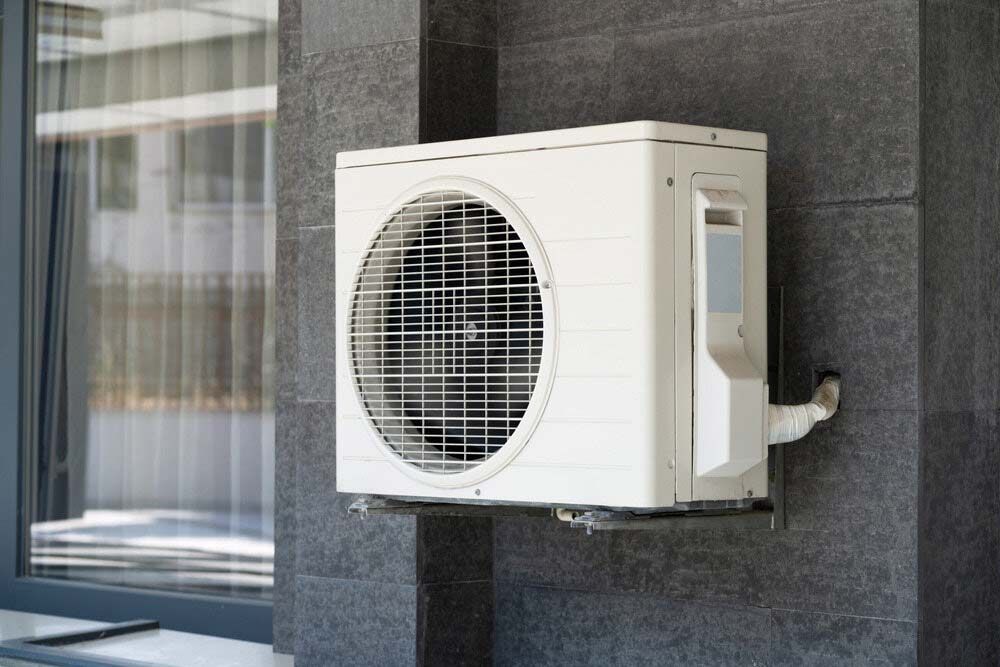 A White Air Conditioner Is Mounted On The Side Of A Building Next To A Window — IPOWER Industries In Cannonvale, QLD