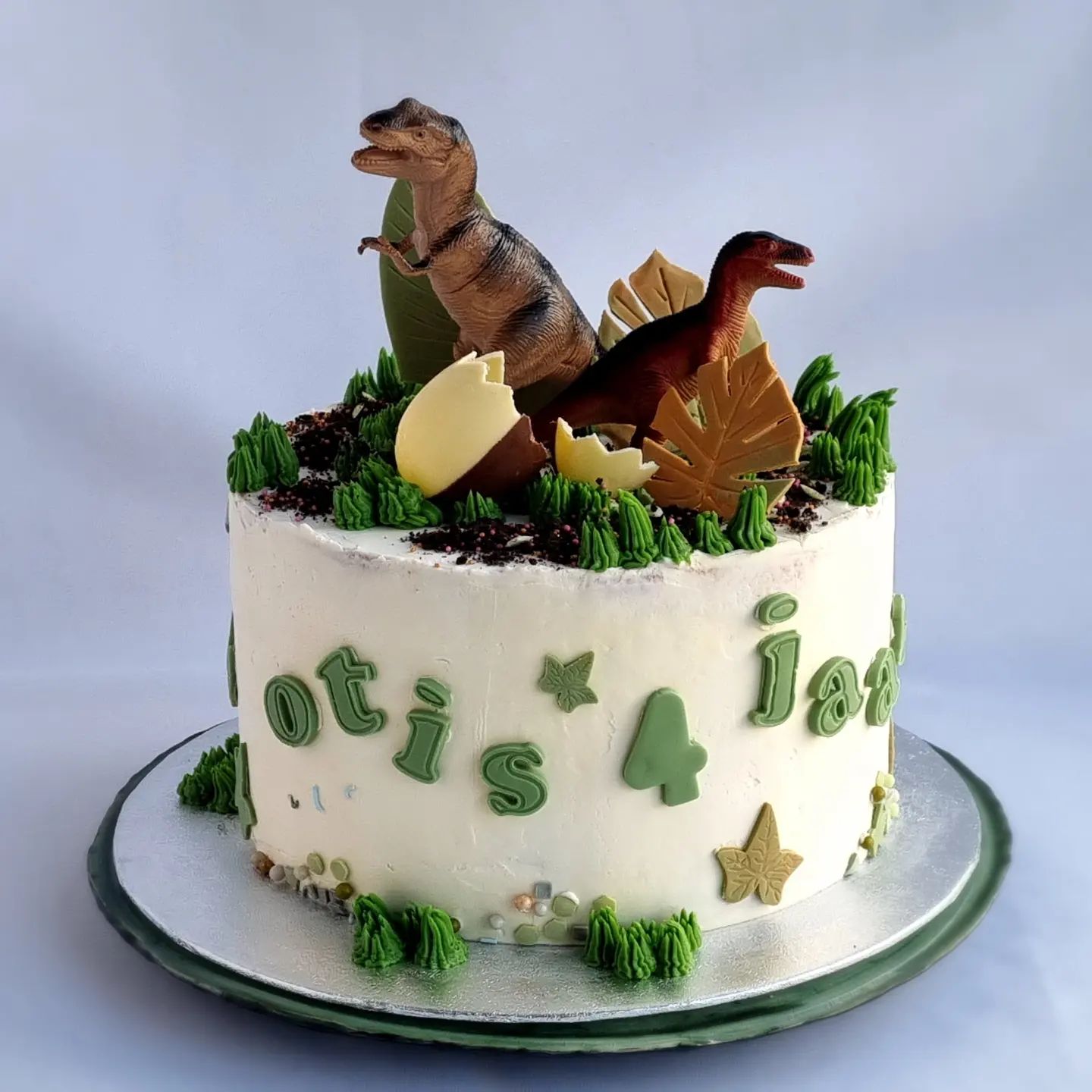 Een verjaardagstaart met dinosaurussen en de naam en leeftijd erop
