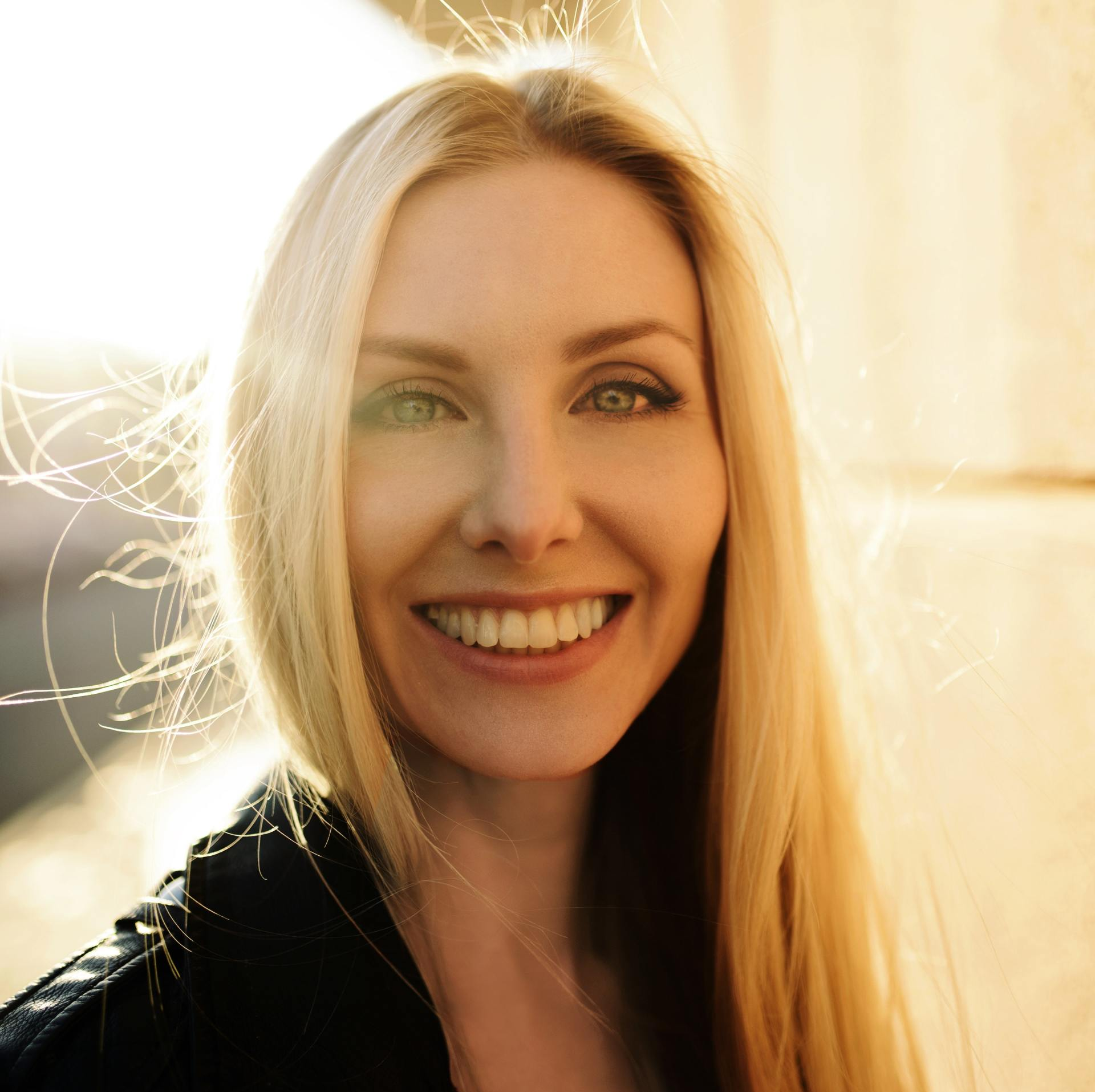 A woman with long blonde hair is smiling and wearing a black jacket