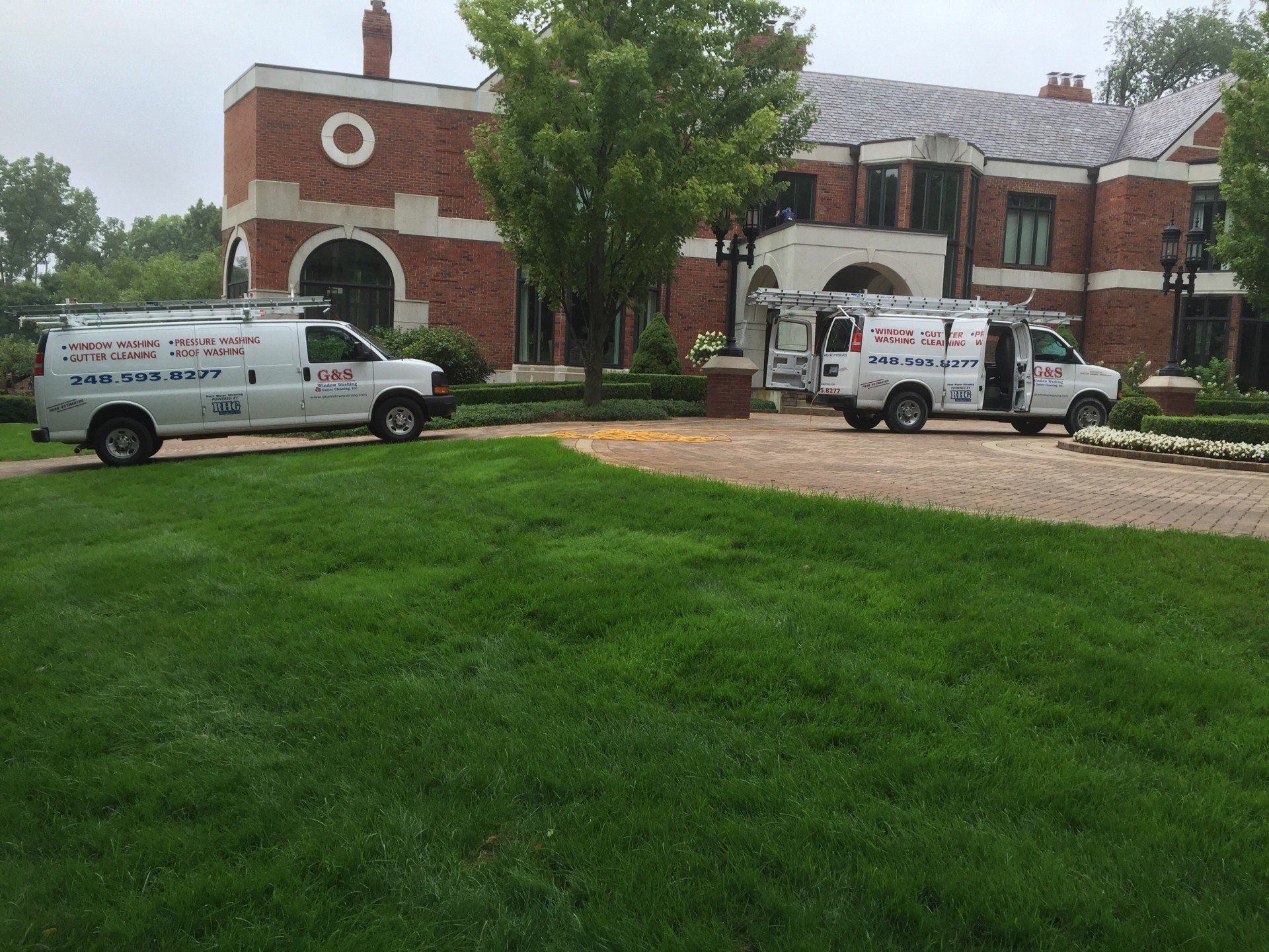 Two white vans are parked in front of a large brick building.
