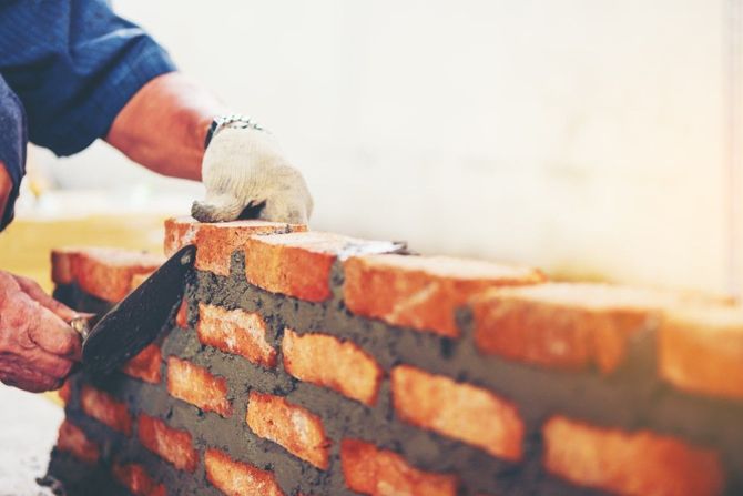 Worker laying red bricks in a wall with mortar