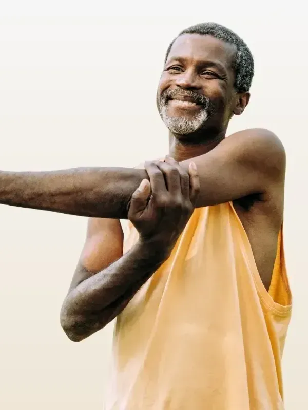 A man in a yellow tank top is stretching his arms and smiling.