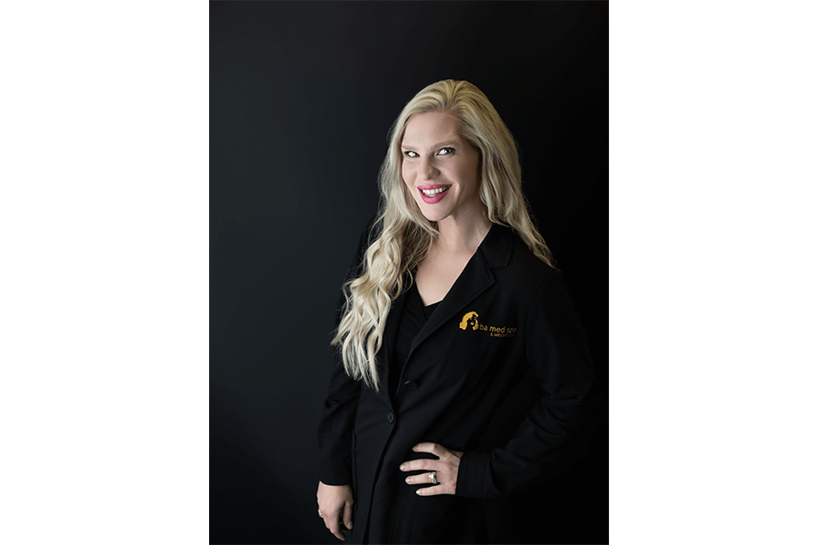 A woman in a black coat is standing in front of a black wall.