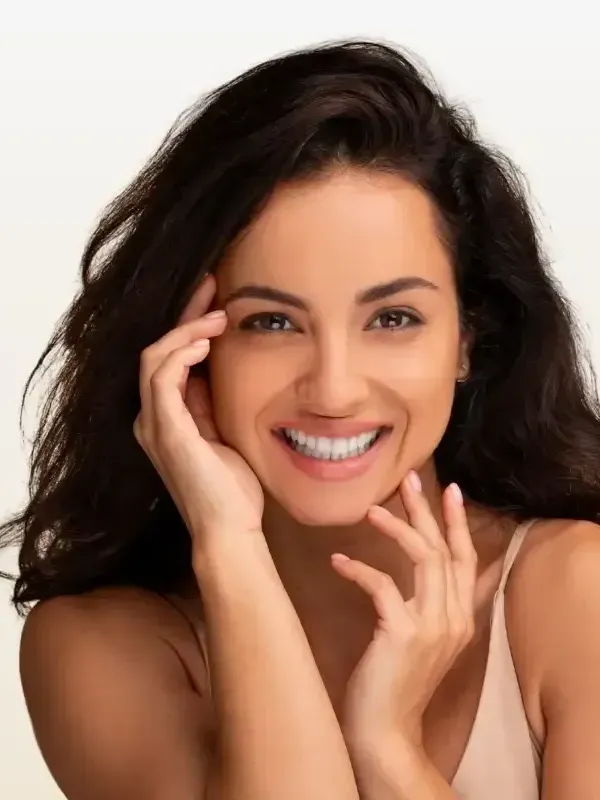 A woman is smiling and touching her face with her hands.