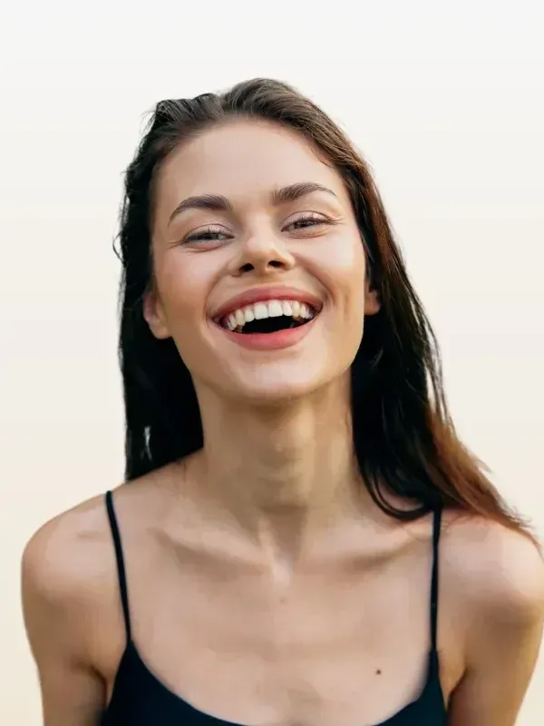 A woman in a black tank top is laughing with her mouth open.