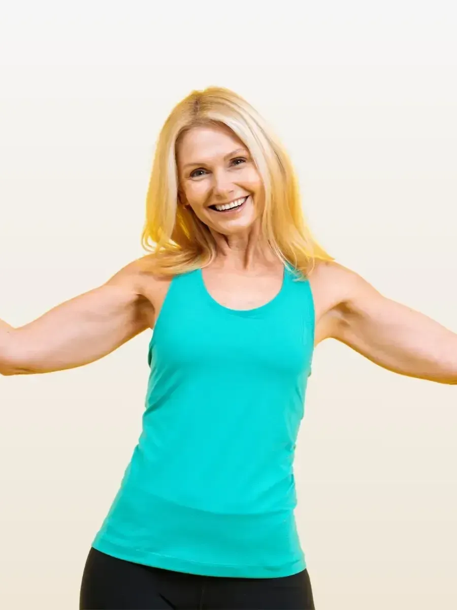 A woman in a blue tank top is smiling with her arms outstretched.