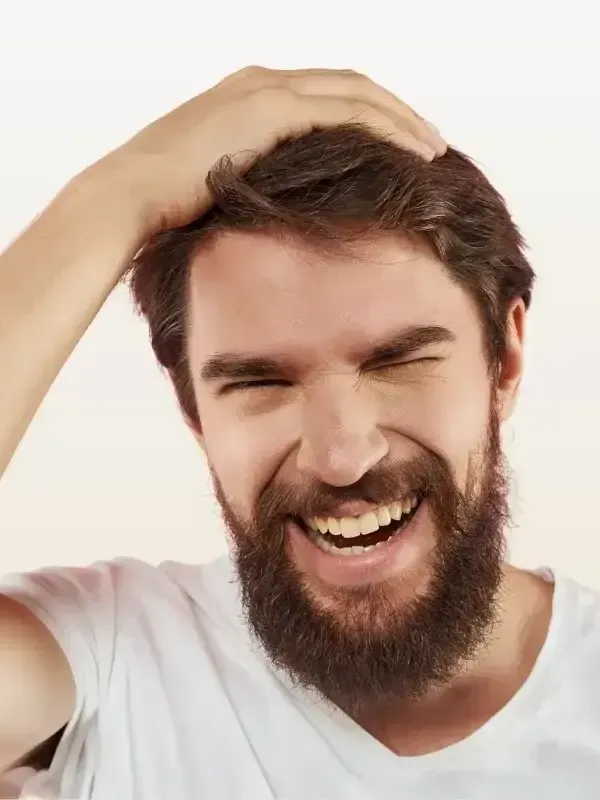 A man with a beard is laughing and touching his hair.