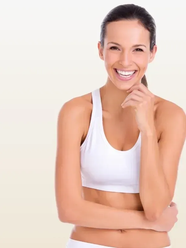 A woman in a white sports bra is smiling with her arms crossed.