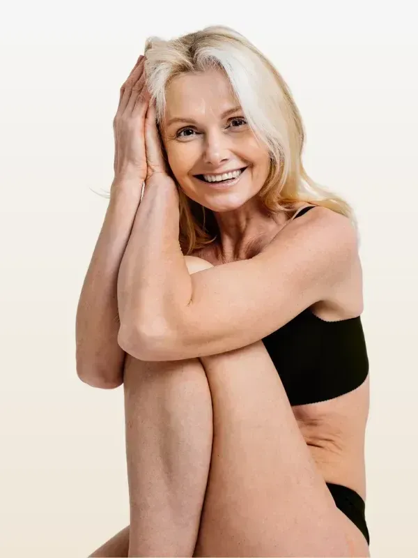 A woman in underwear is sitting with her legs crossed and smiling.