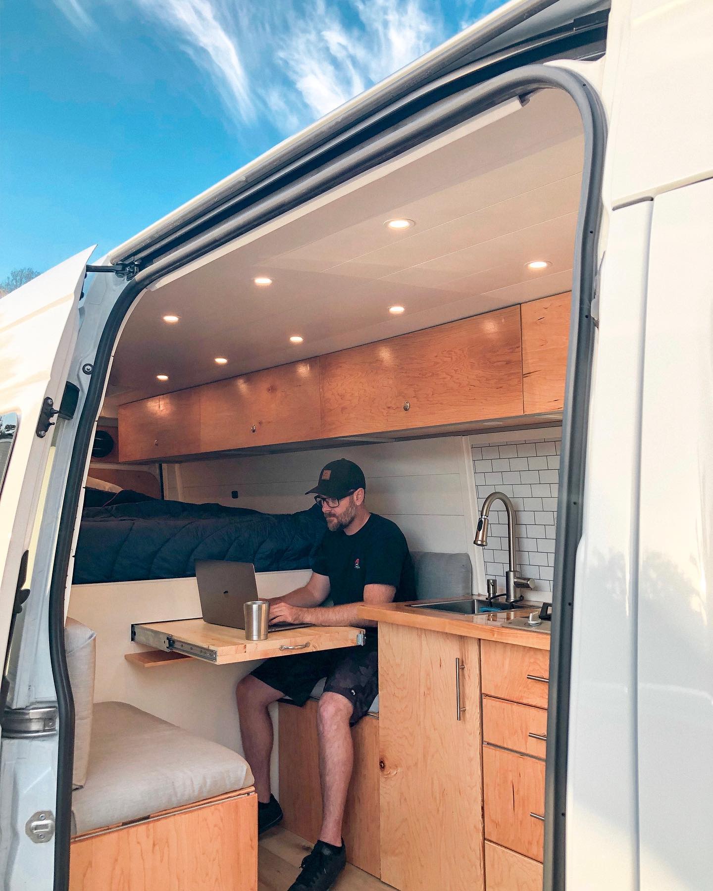 a man is sitting at a table in a van using a laptop .