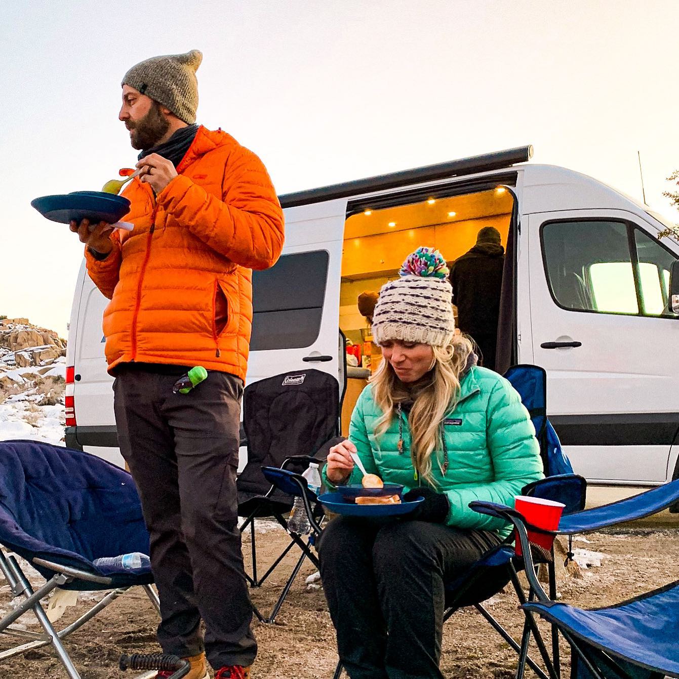a man and a woman are eating food in front of a van .