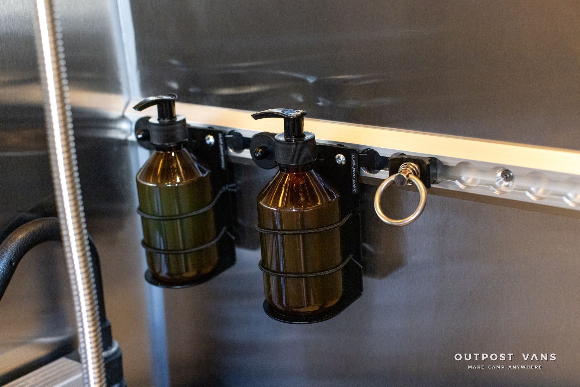 Two bottles of soap are hanging on a metal wall.