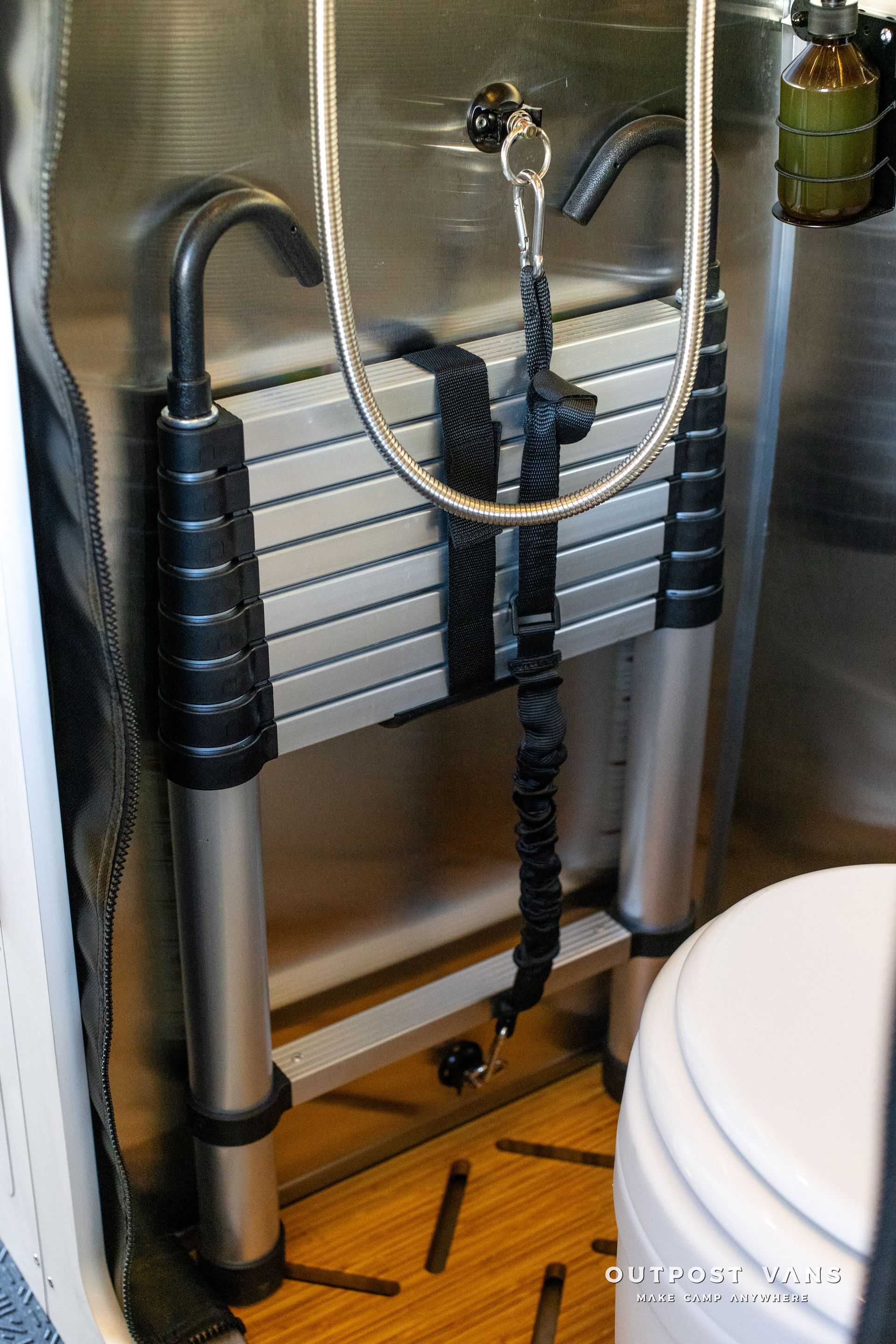 A bathroom with a toilet and a ladder with a hose attached to it.