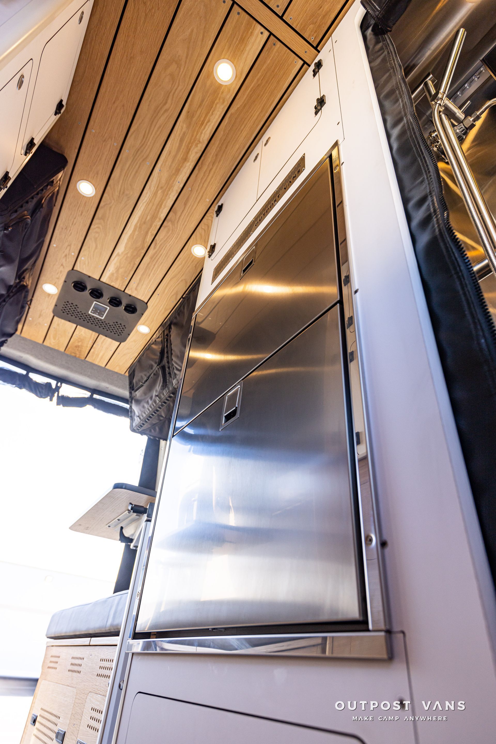 A stainless steel refrigerator in a van with a wooden ceiling.