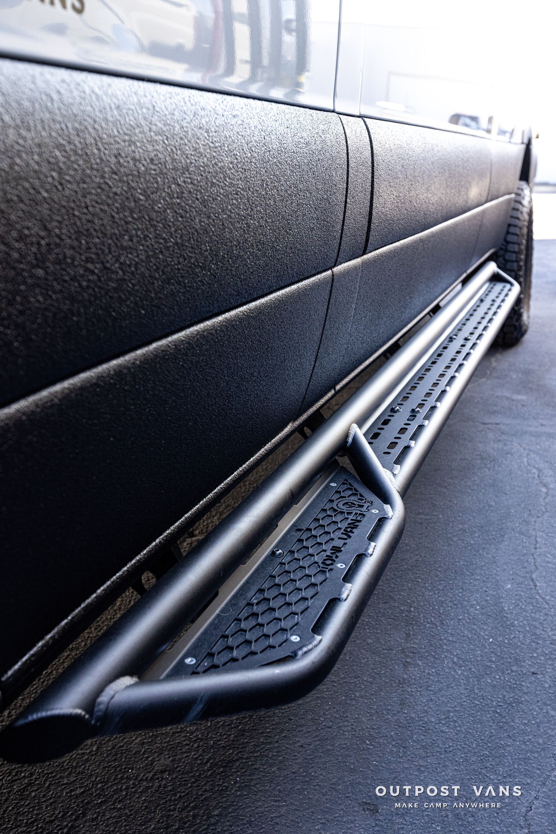 A black truck with side steps on it is parked on the side of the road.