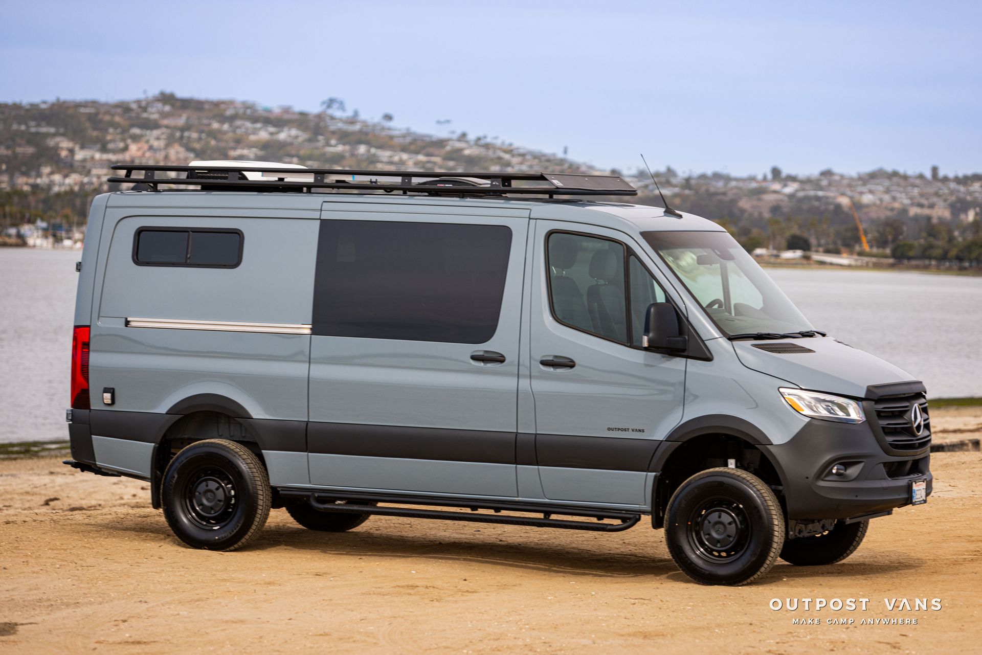 A gray van is parked on a dirt road next to a body of water.