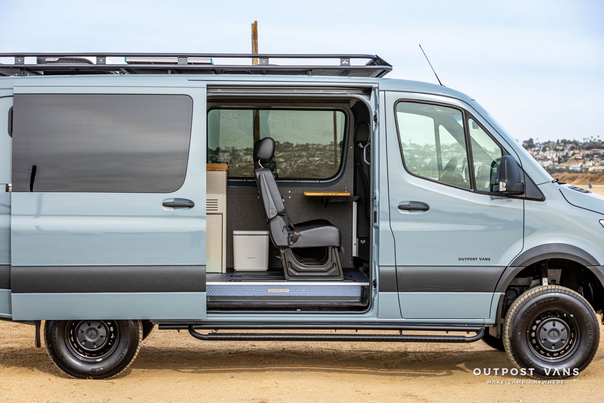 A blue van with the door open is parked in the dirt.