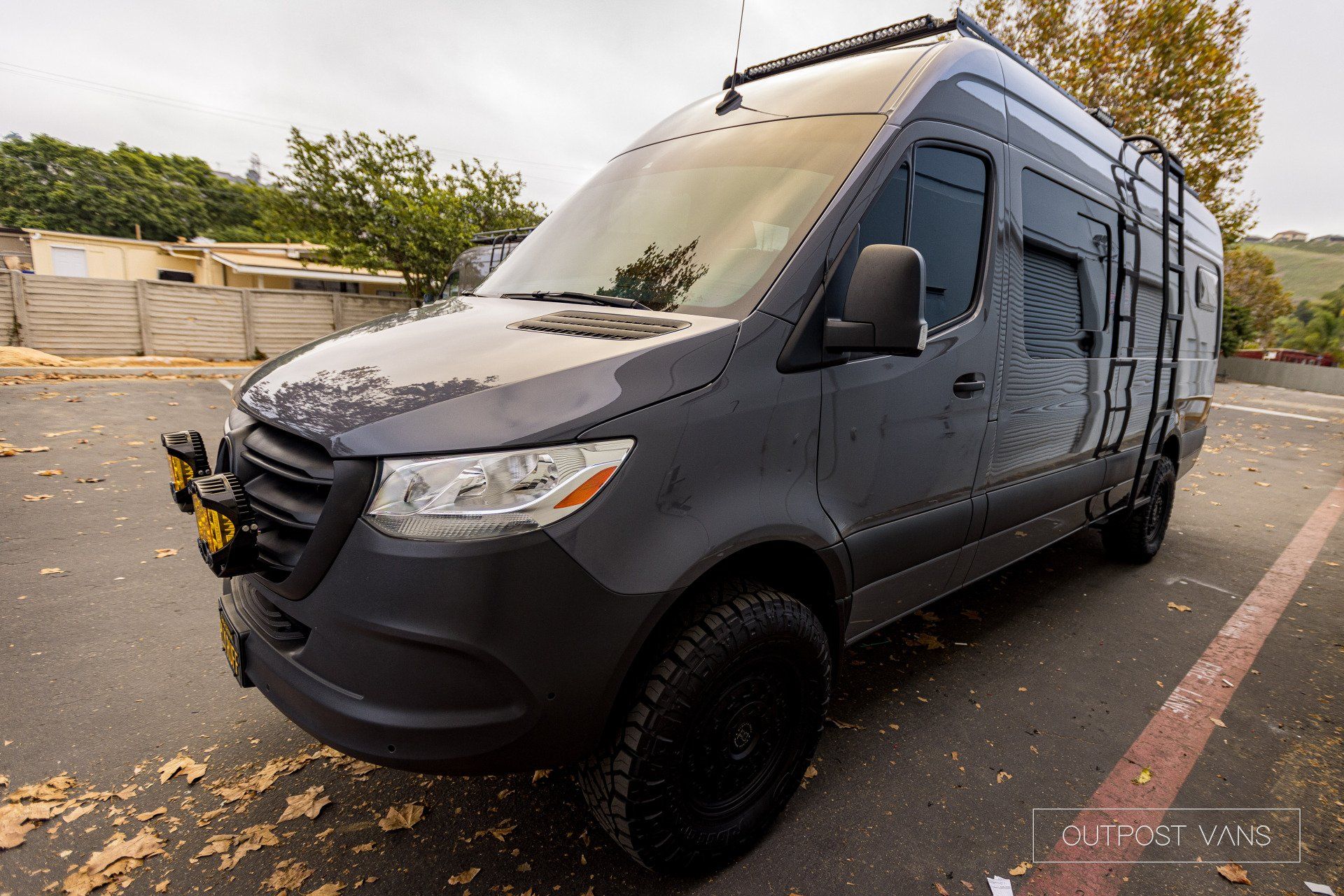 a black van with a ladder on the roof is parked in a parking lot .