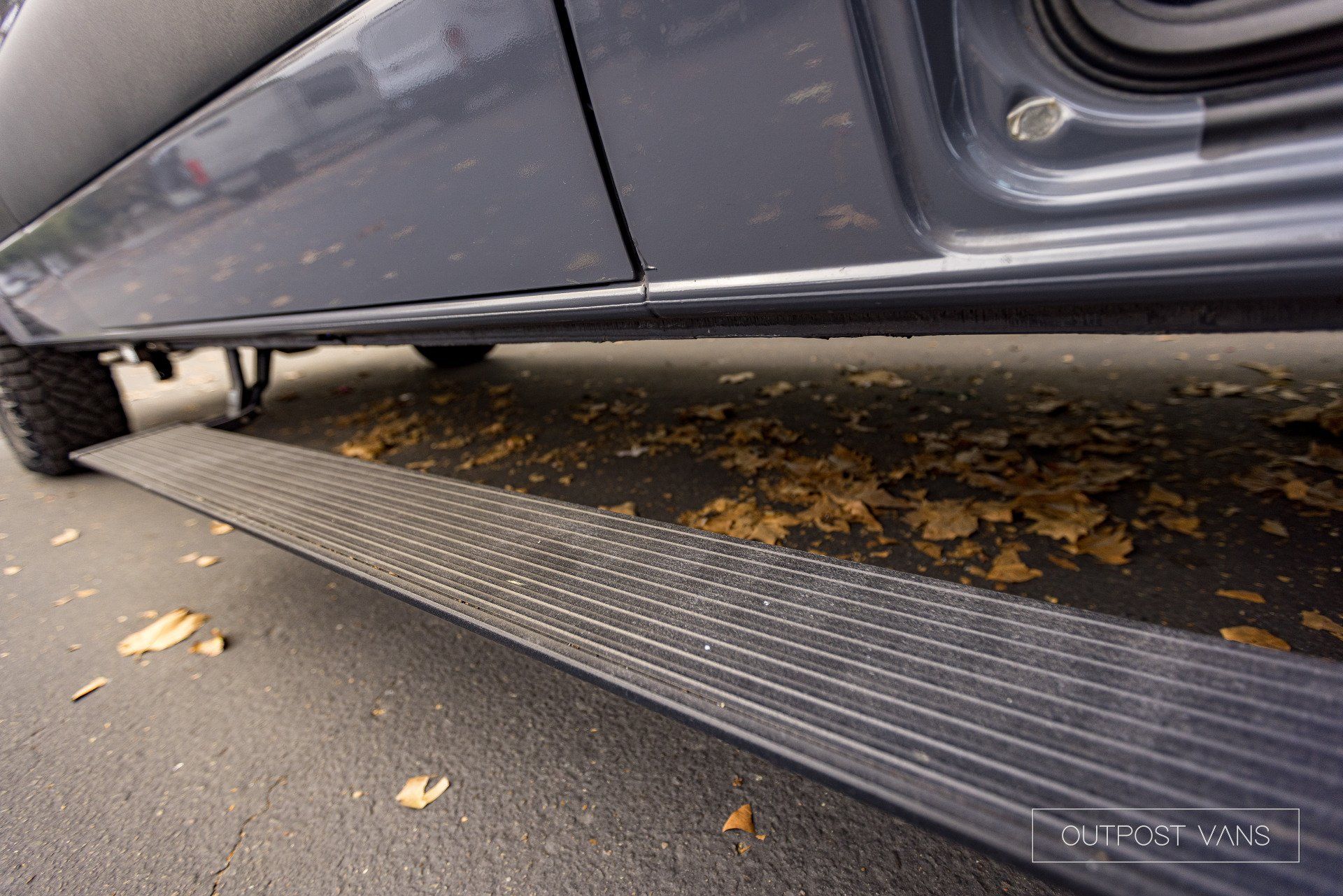A close up of the side of a car with leaves on the ground.