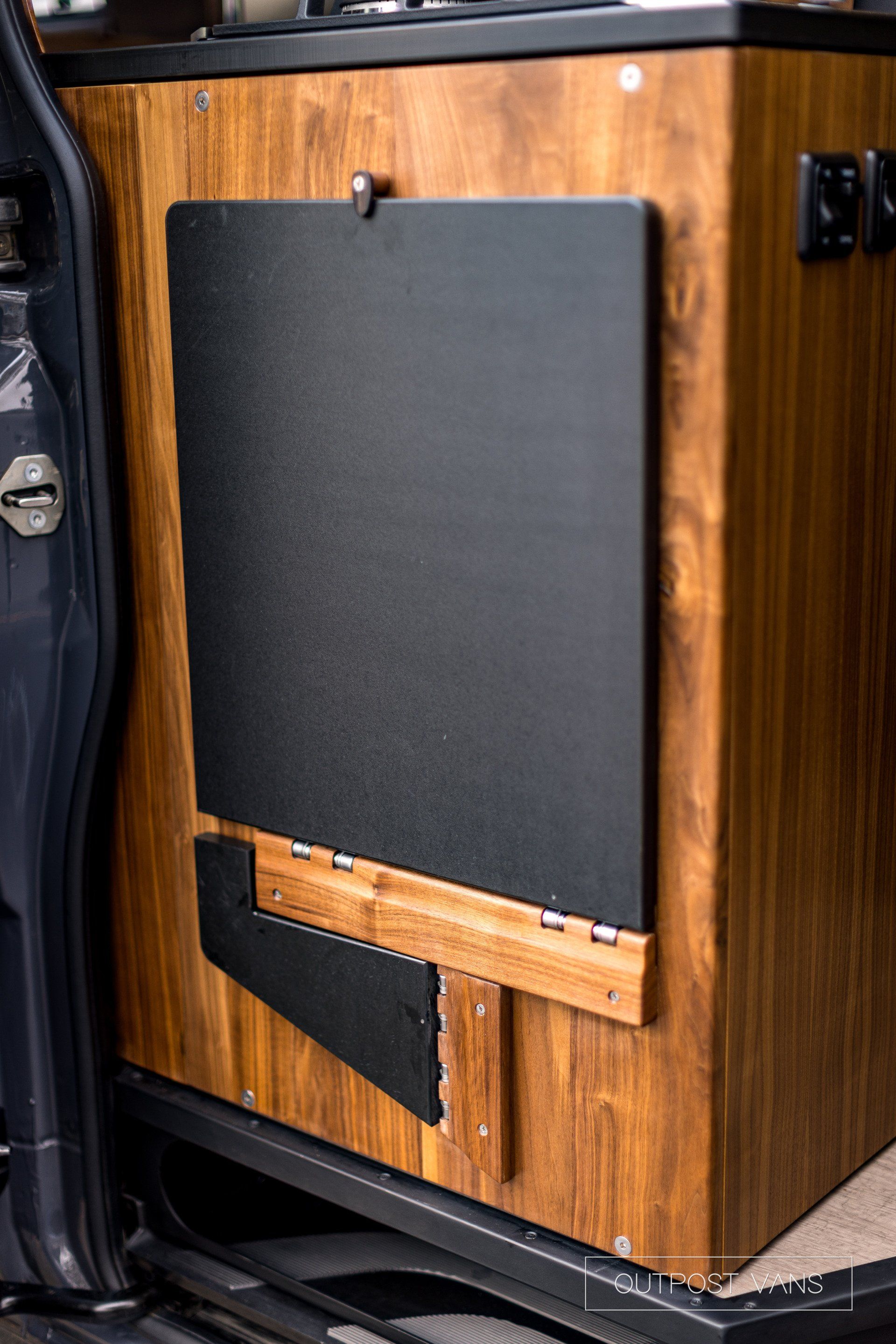 A wooden cabinet with a black door is sitting in the back of a van.