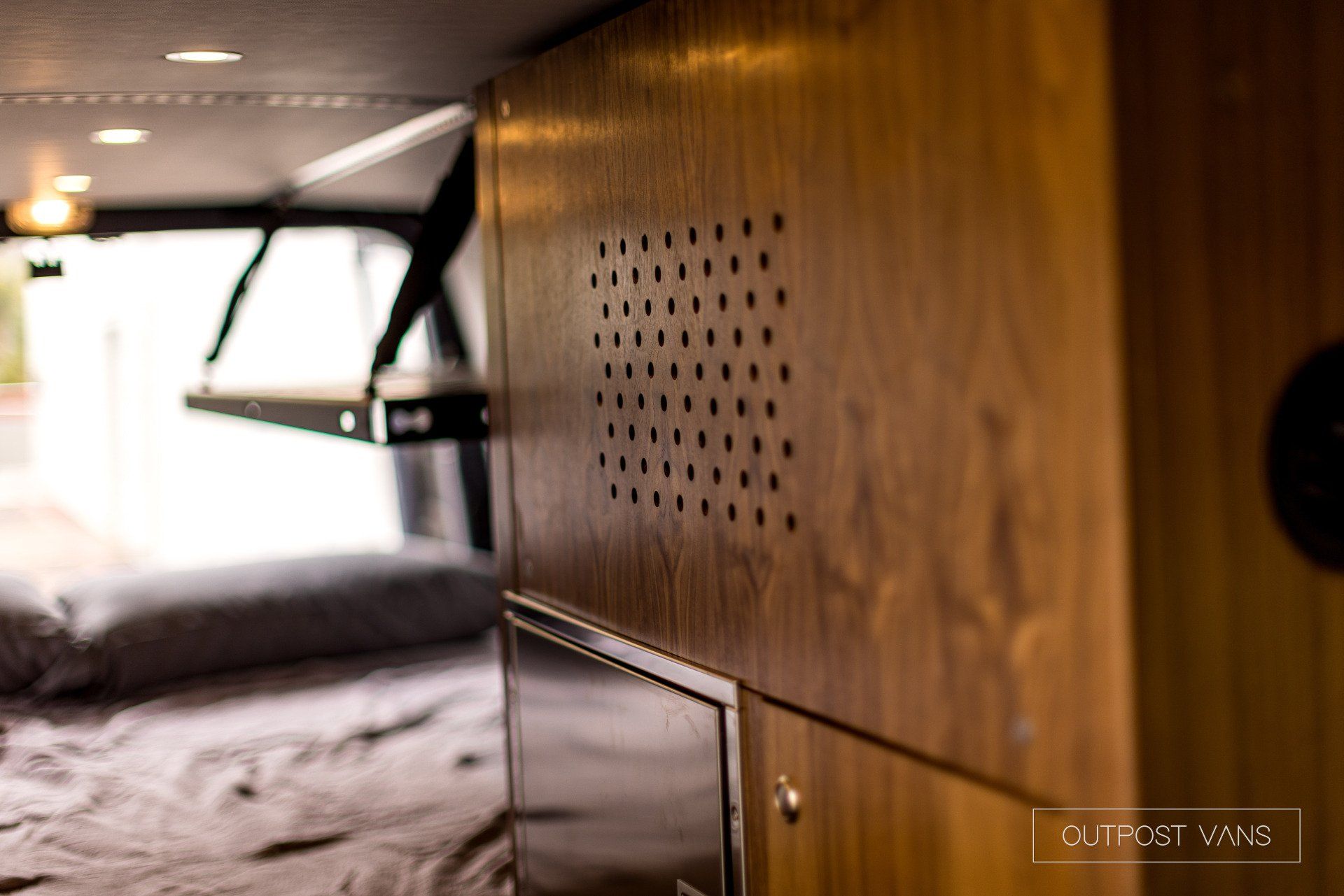 A wooden box with holes in it is sitting next to a bed in a van.