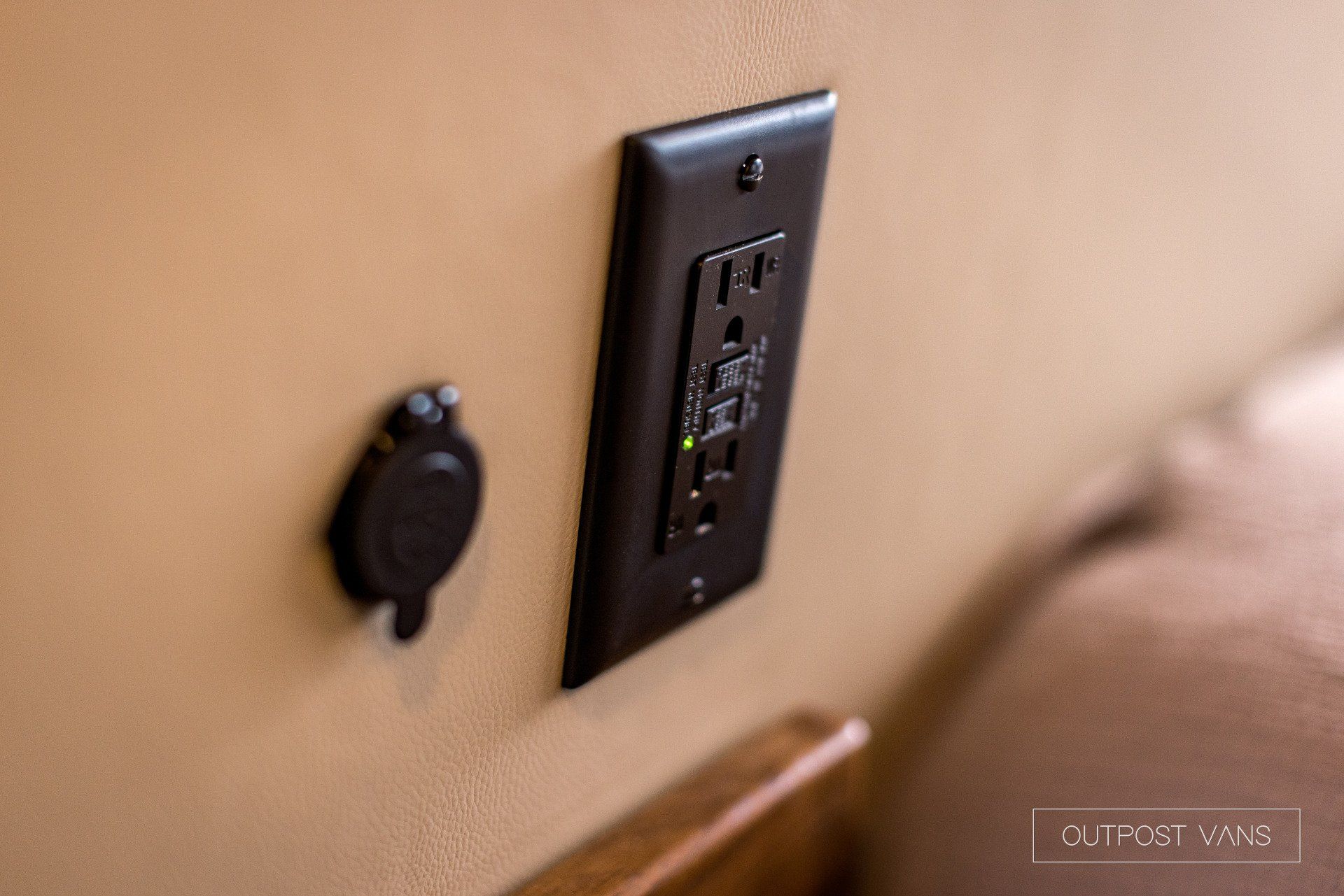A close up of an electrical outlet on a wall next to a bed.