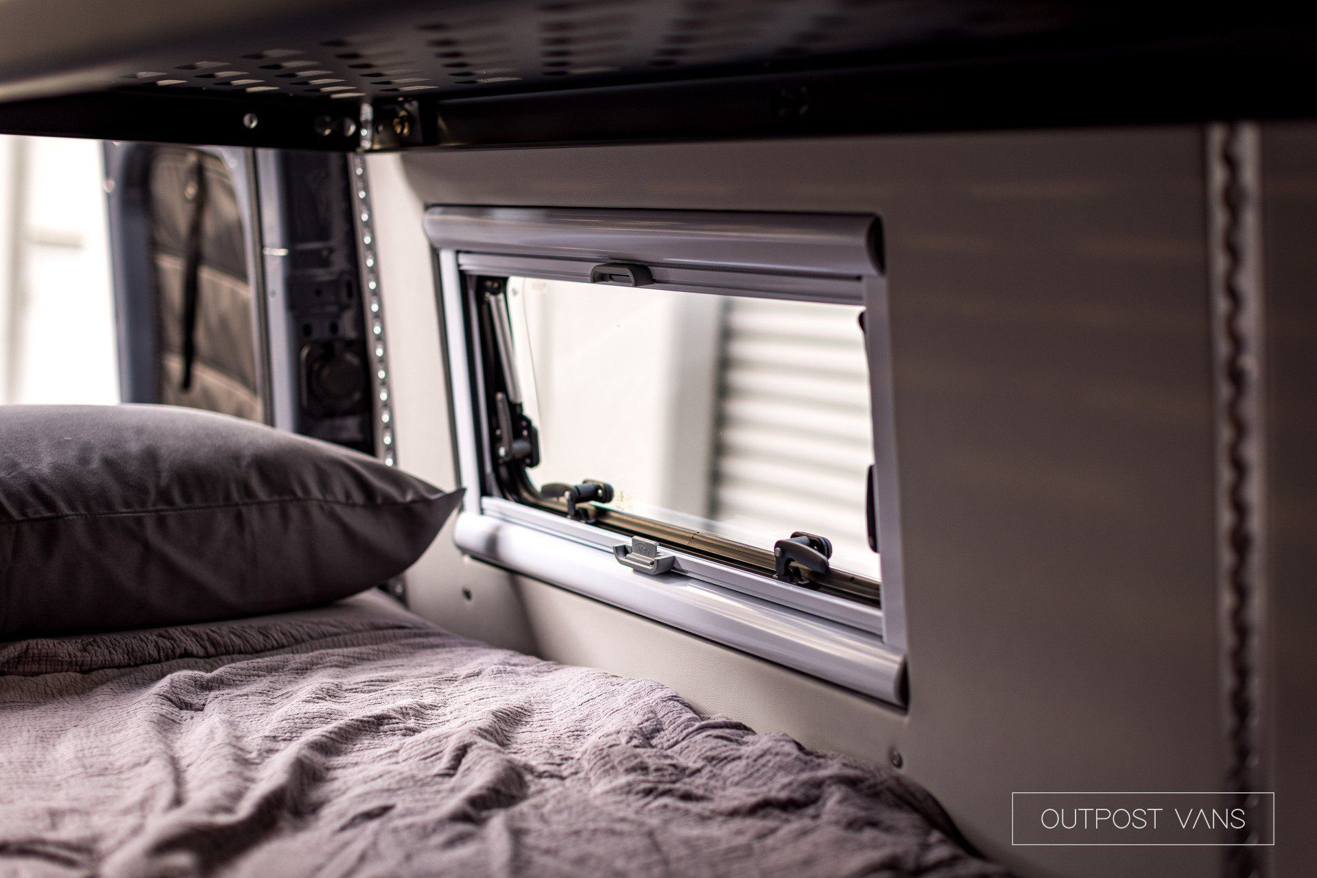 A bed with a pillow and a window in a camper van.