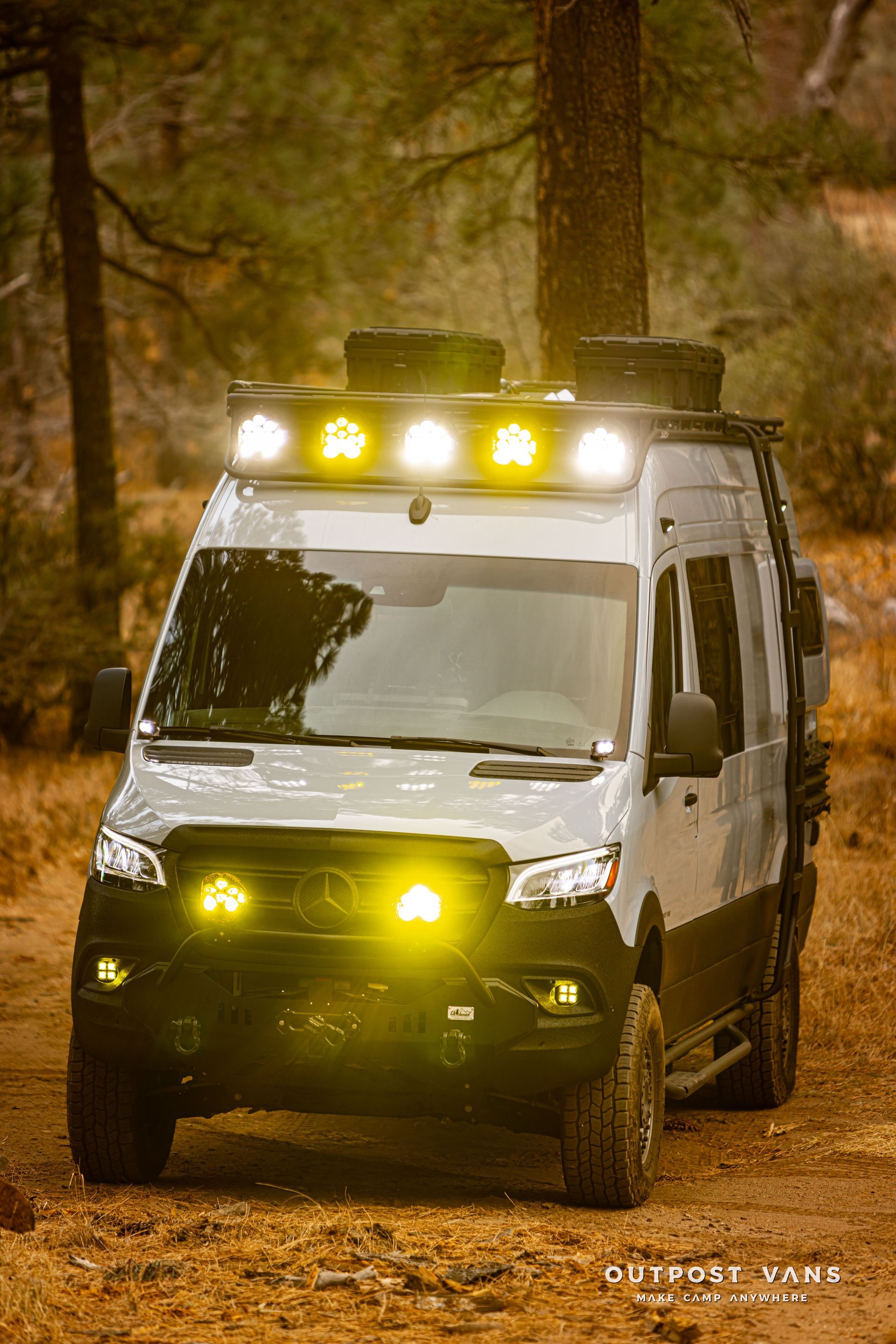 A white van with yellow lights on the roof is driving down a dirt road.