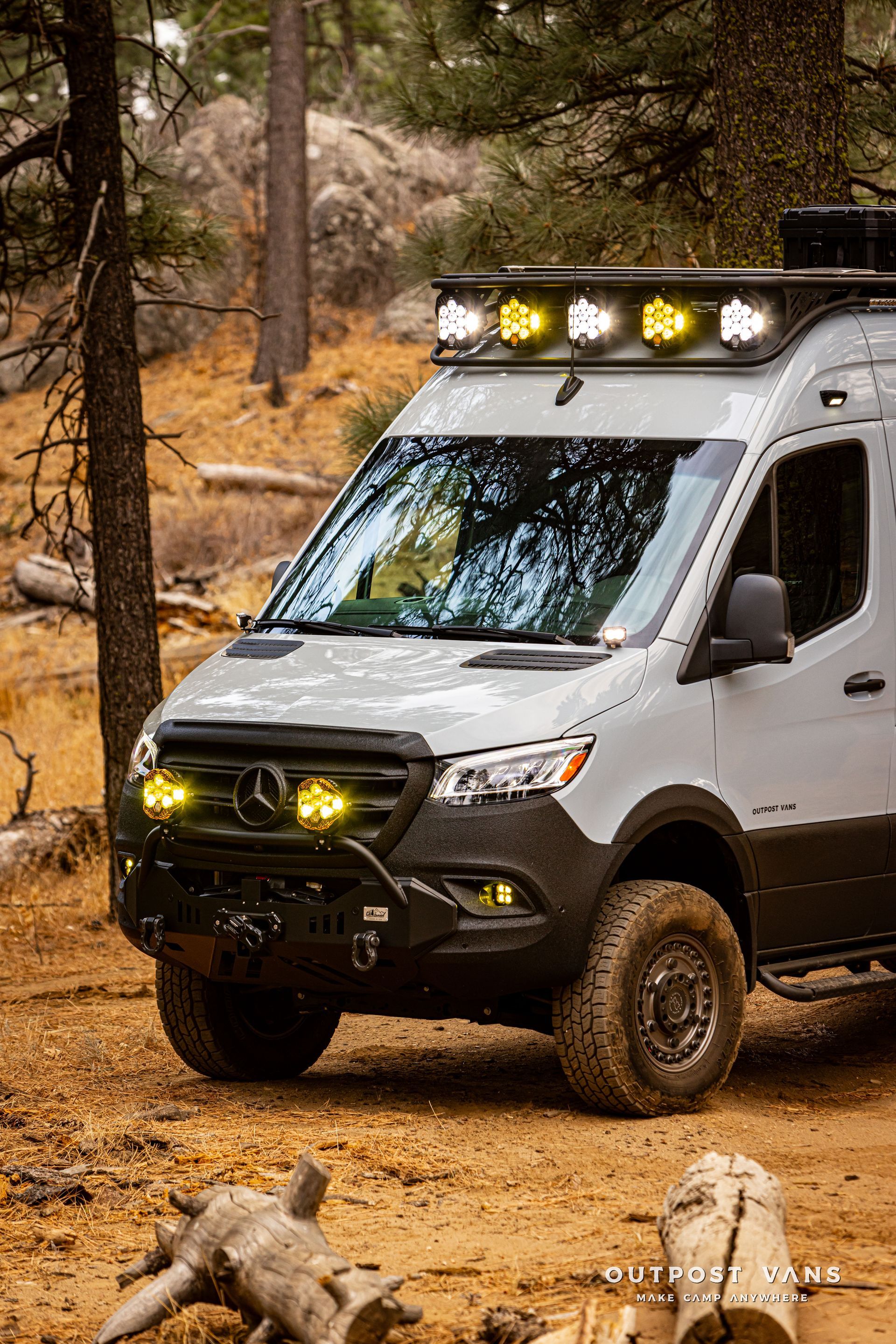 A white van is parked in the dirt in the woods.