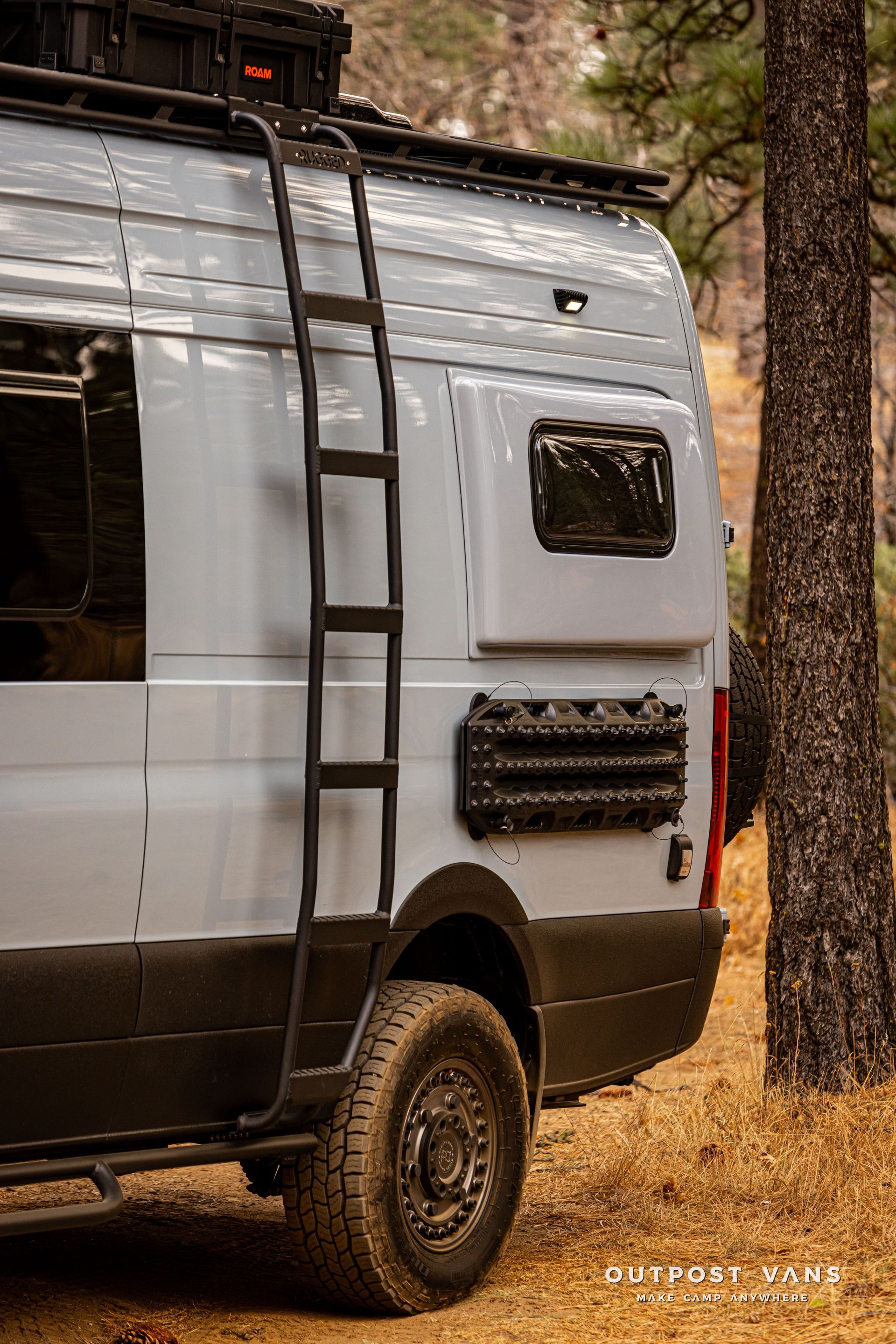 A van with a ladder on the back is parked next to a tree.
