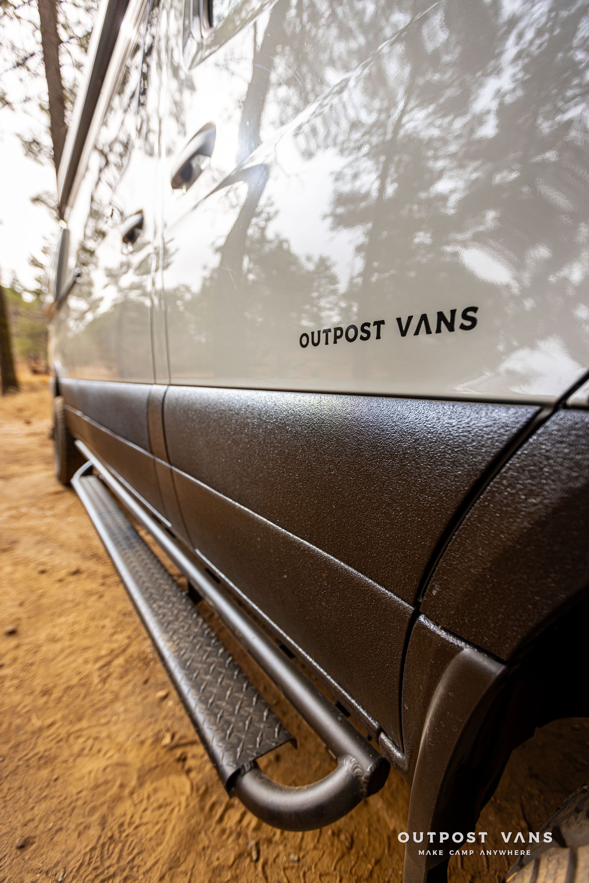 A white van with black side steps is parked in the dirt.