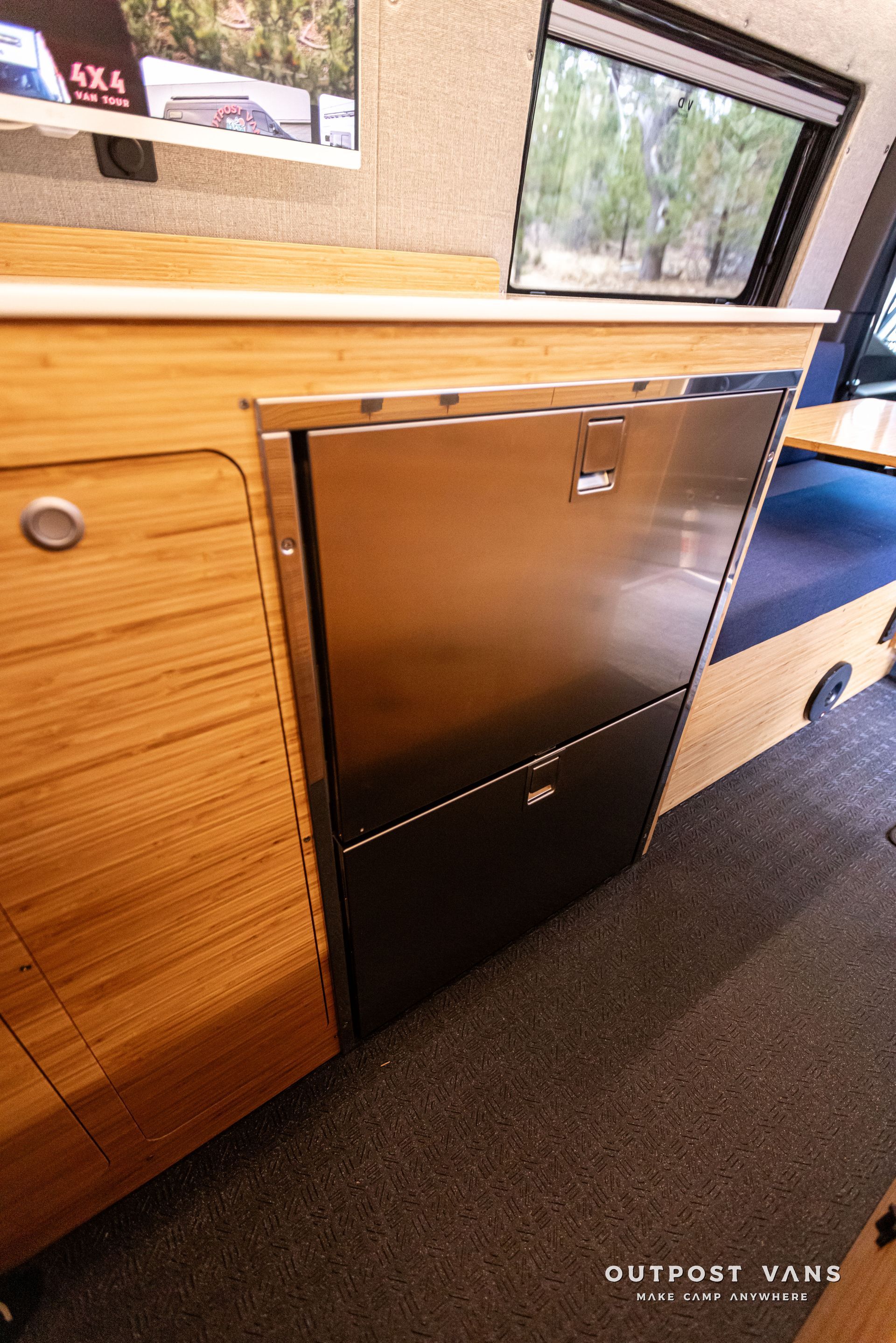 A stainless steel refrigerator is sitting under a wooden cabinet in a van.