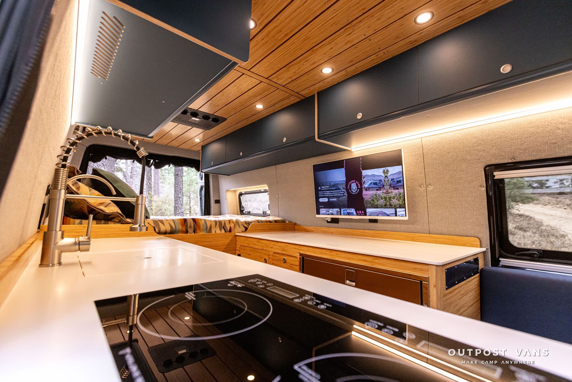 A kitchen in a van with a stove top oven and a television.