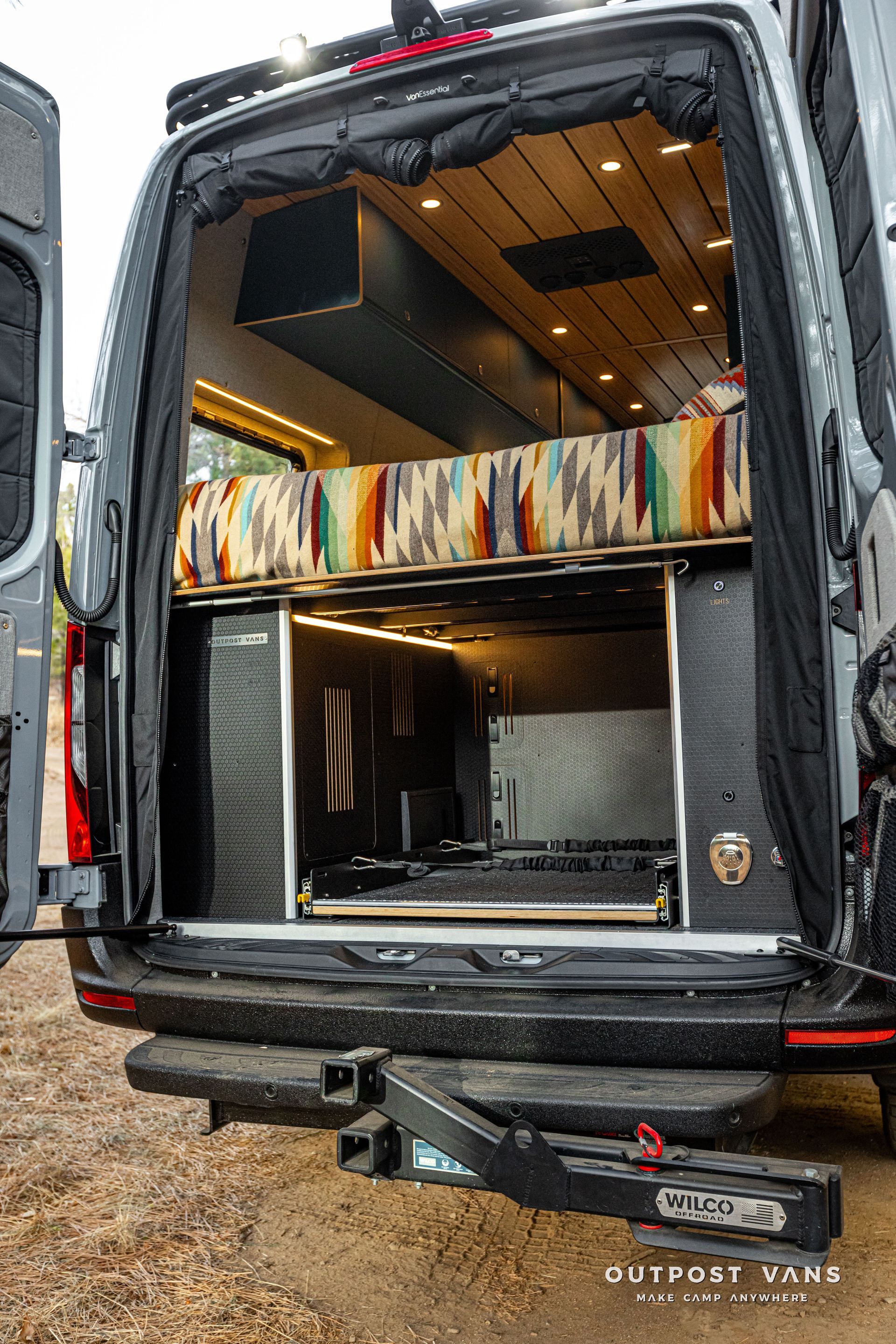 The back of a van with the door open and a bed in the back.