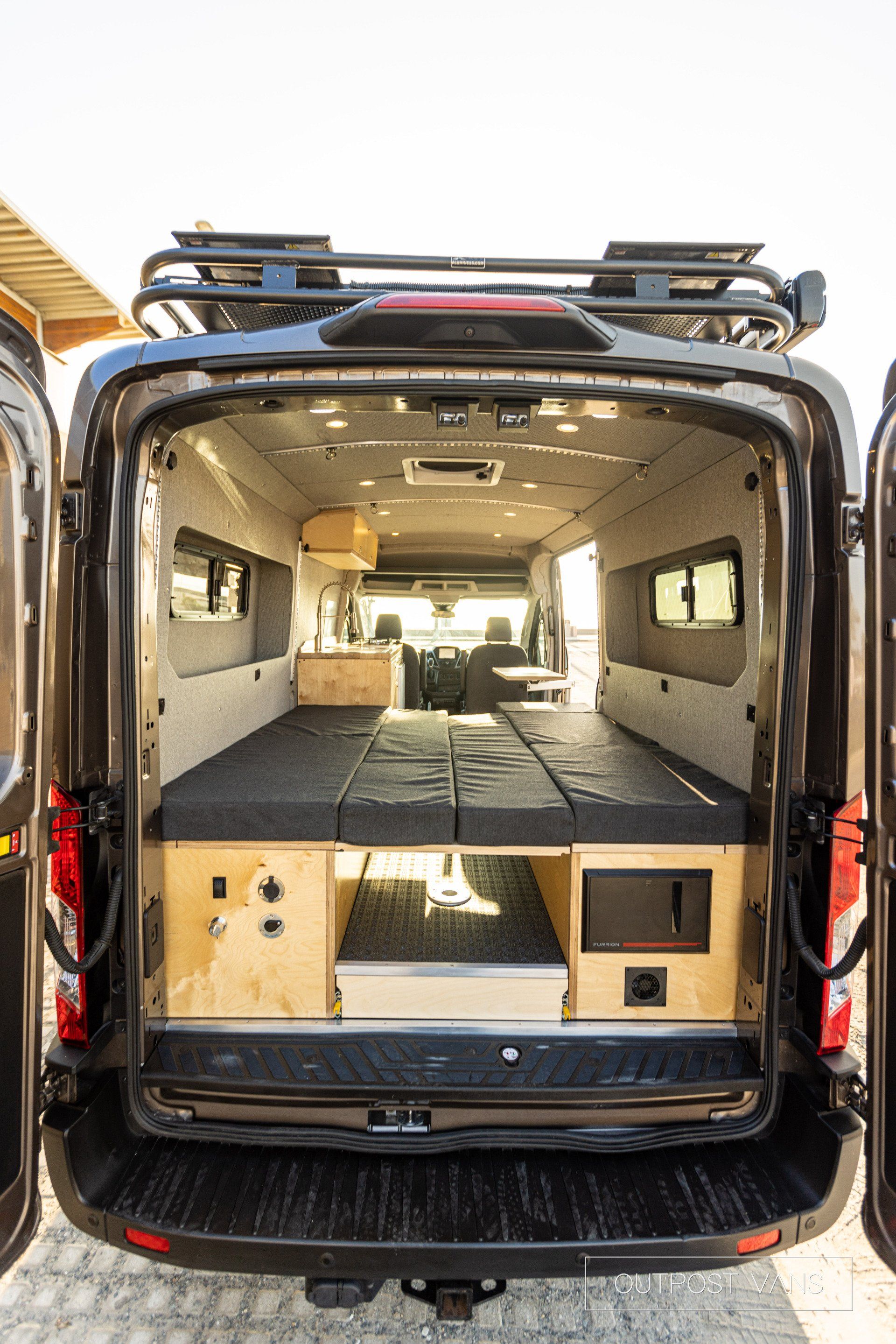 the back of a van with its doors open and a bed in the back .