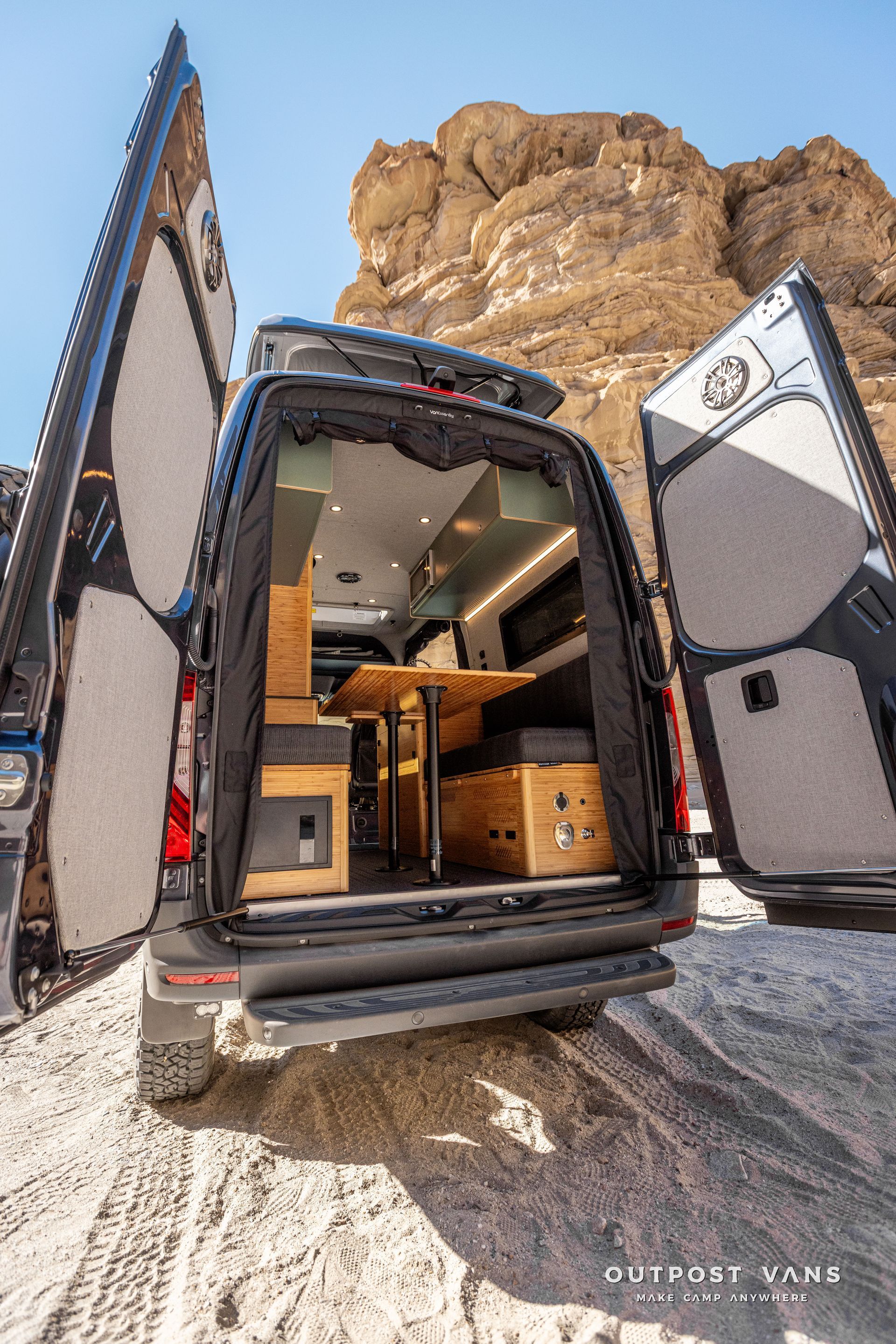 The inside of a camper van with a dinette table and benches that convert to a bed. outdoor shower