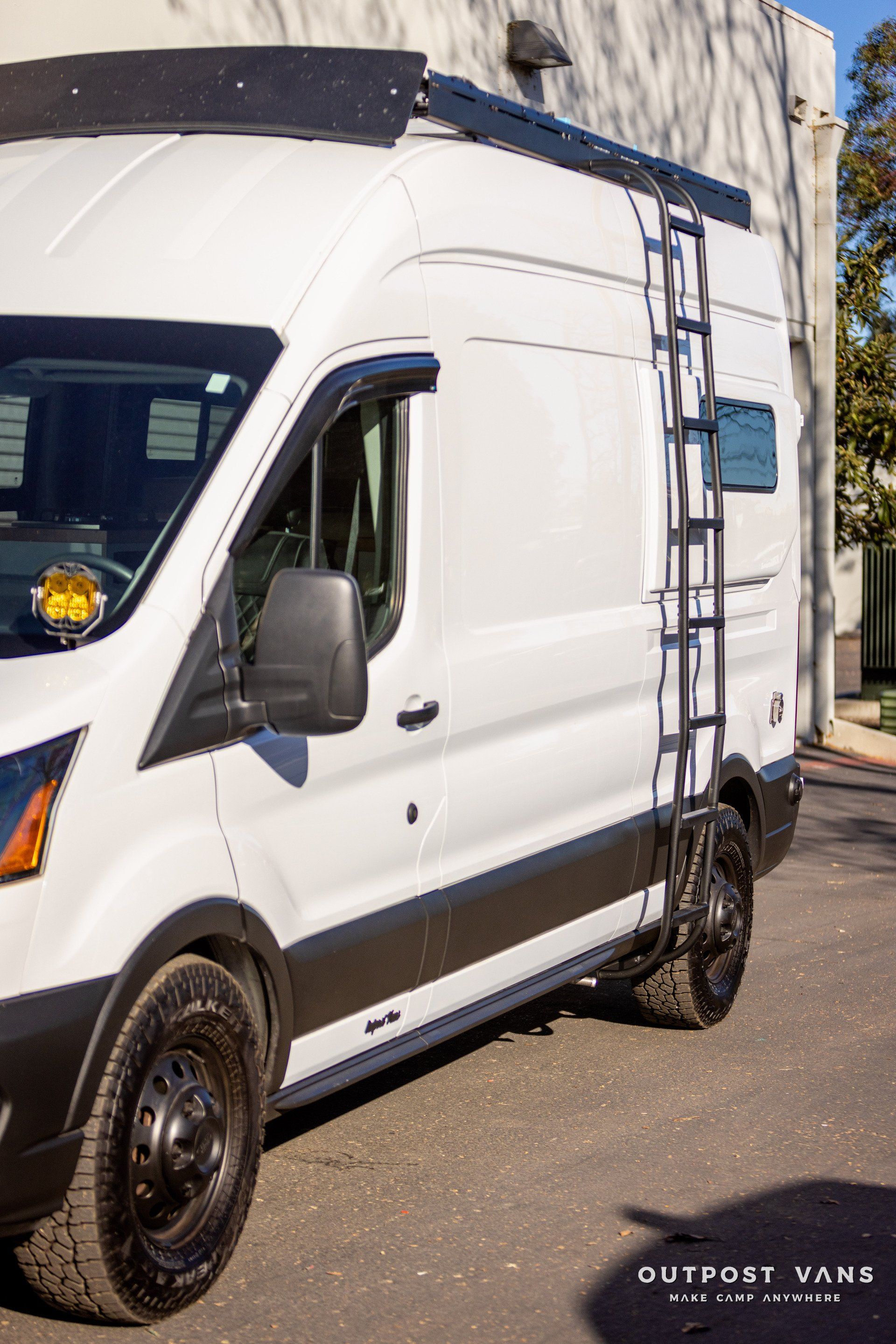 a white van with a ladder attached to the side is parked in front of a building .