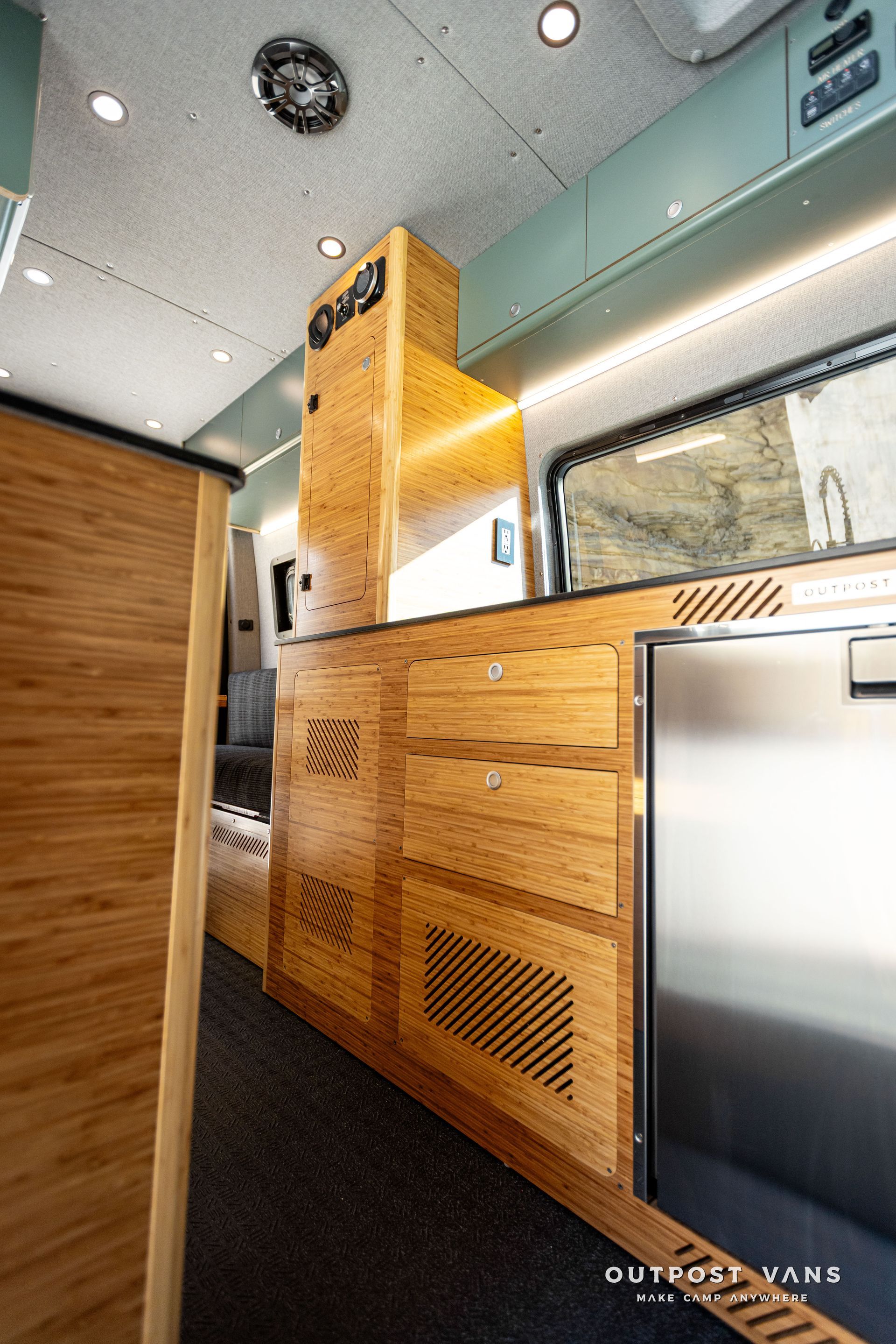 A kitchen in a van with wooden cabinets and stainless steel appliances.
